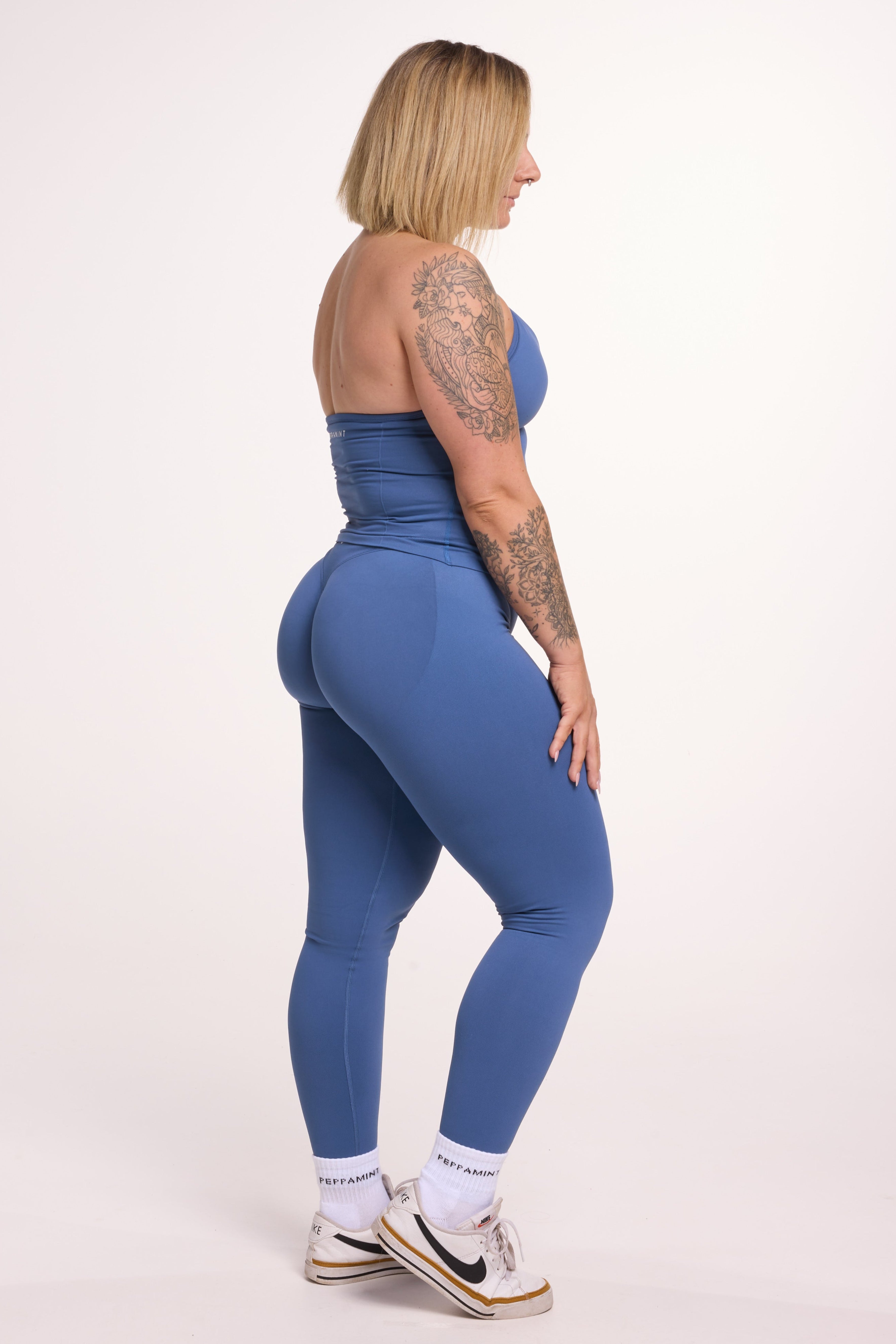 Halter neck tank top with breast contouring panels and a ruched front seam, a built in bra, and an open upper back design and seamless gym tights with booty contouring panels, invisible scrunch technology, sweetheart shaped back seams and thick supportive fabrics in grey blue colour