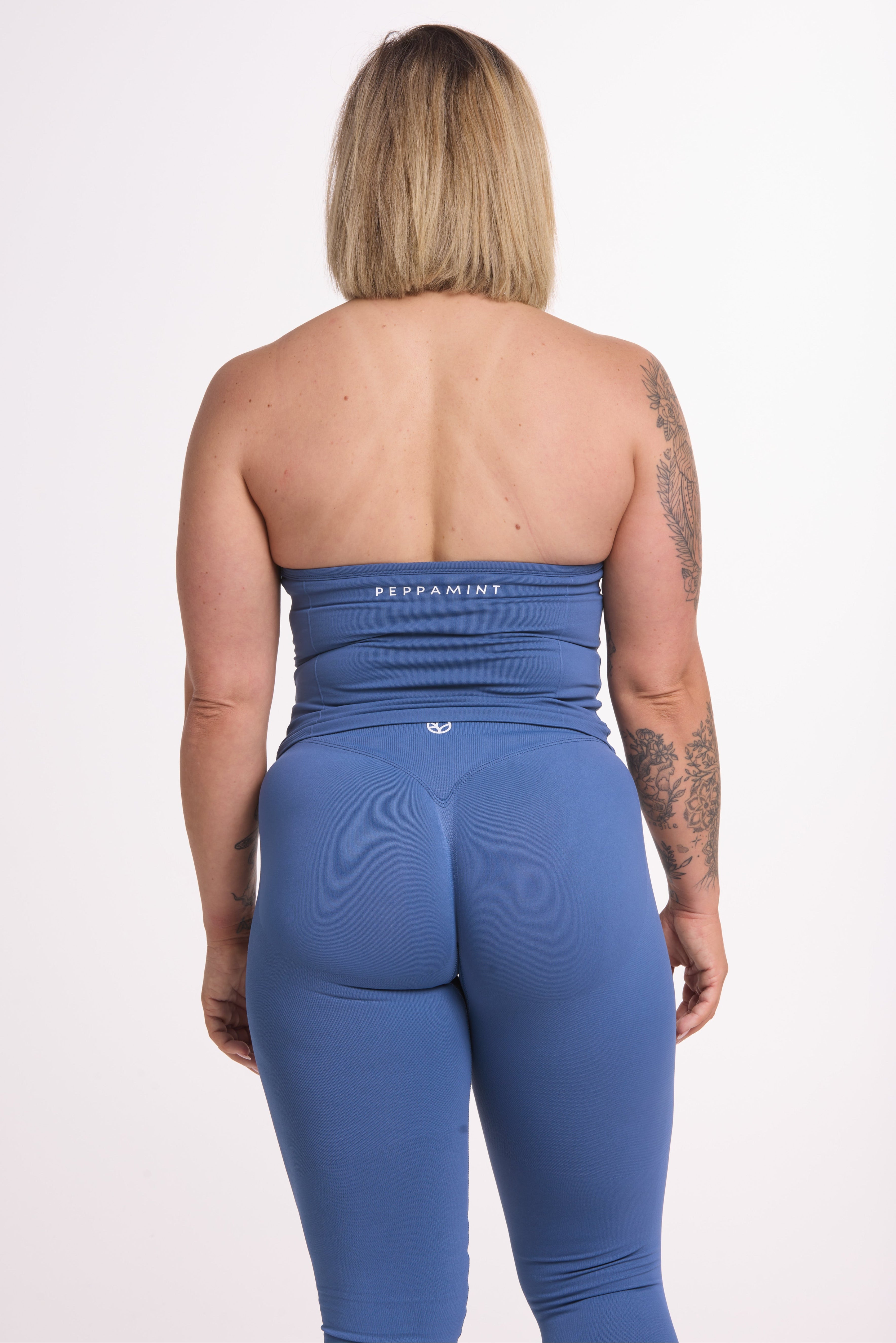 Halter neck tank top with breast contouring panels and a ruched front seam, a built in bra, and an open upper back design and seamless gym tights with booty contouring panels, invisible scrunch technology, sweetheart shaped back seams and thick supportive fabrics in grey blue colour