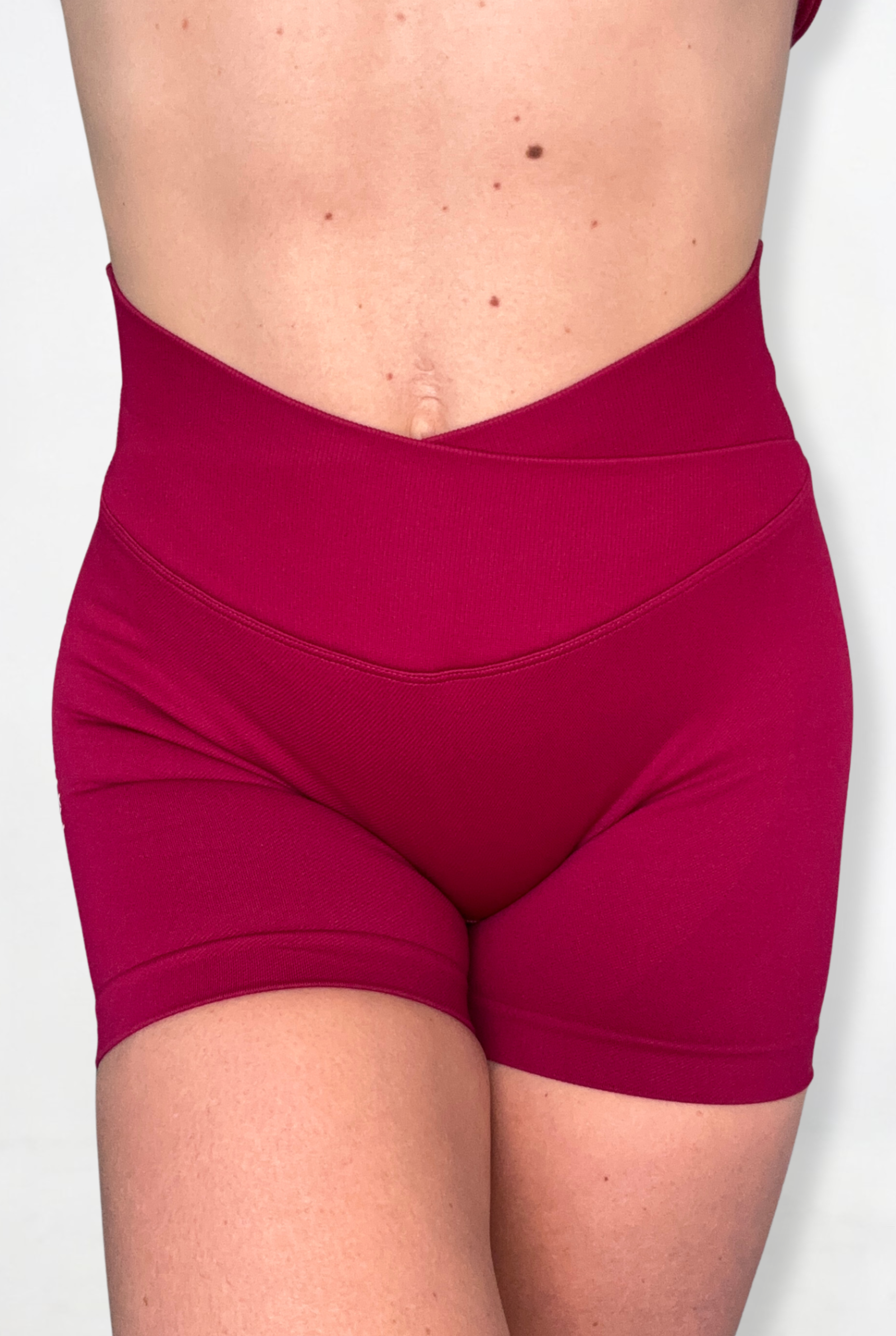 A close-up of a model's lower torso wearing high-waisted magenta athletic V waistband shorts against a plain light background.