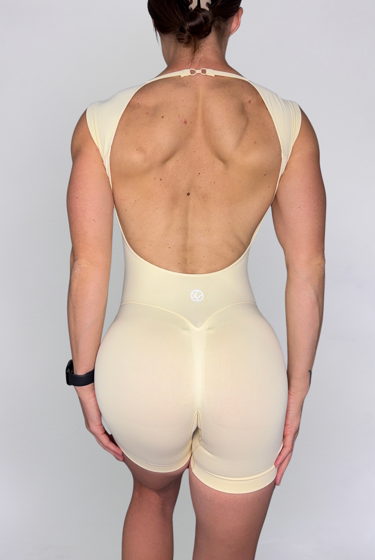 Rear view of a model wearing a Butter Yellow open-back bodysuit against a light grey studio background.
