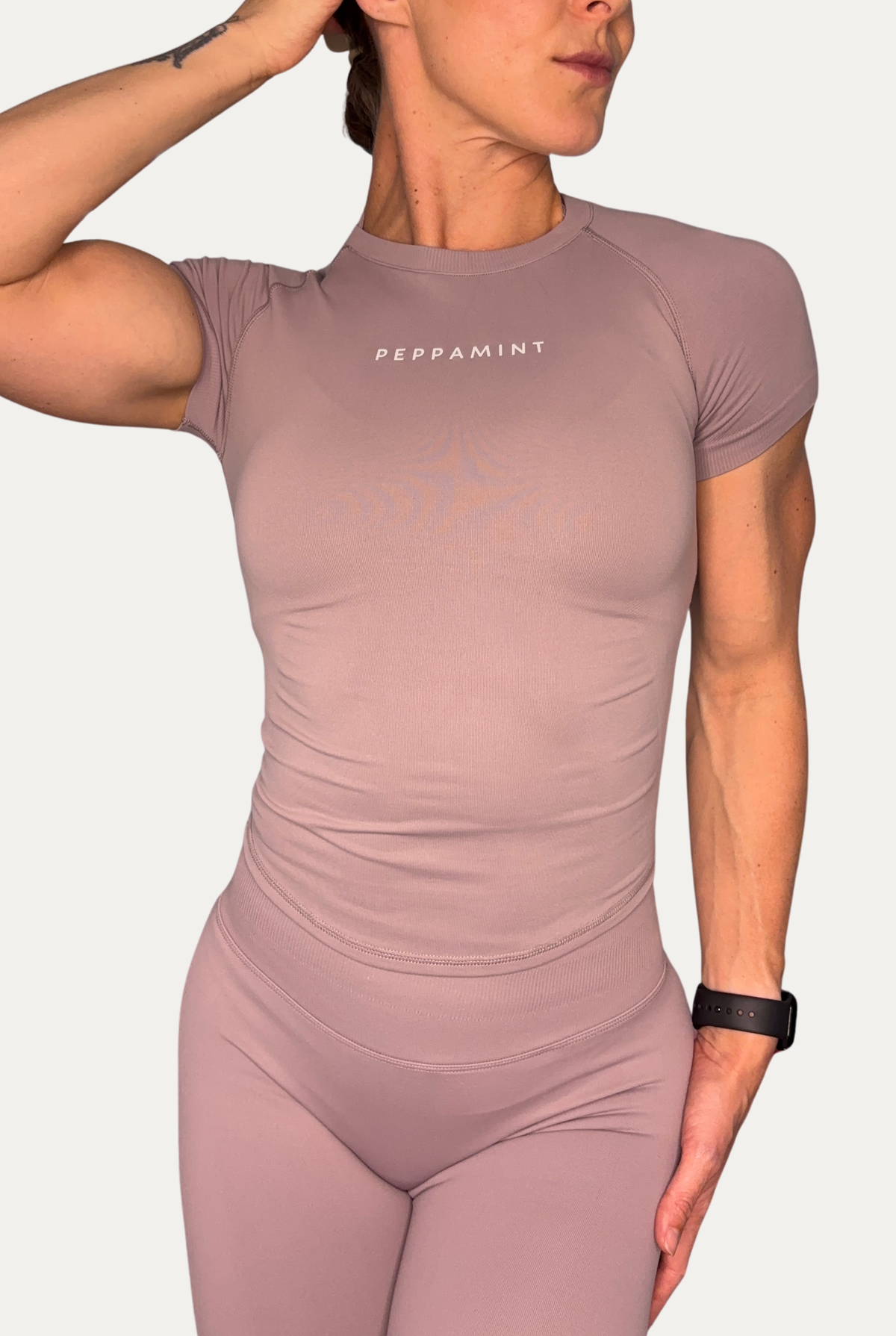 A woman wearing a fitted short-sleeve athletic top and matching leggings in a stone beige colour. The top has the word 'PEPPAMINT' printed in white across the chest.
