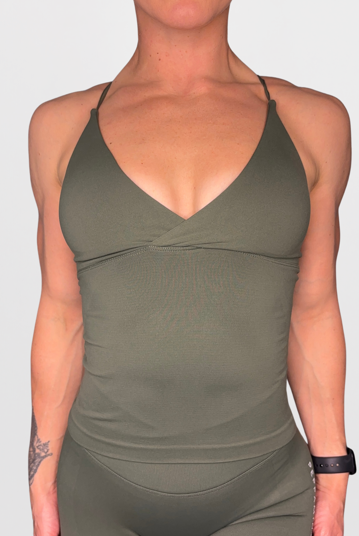 A close-up of a model wearing an olive green athletic tank top and matching leggings against a light grey background.