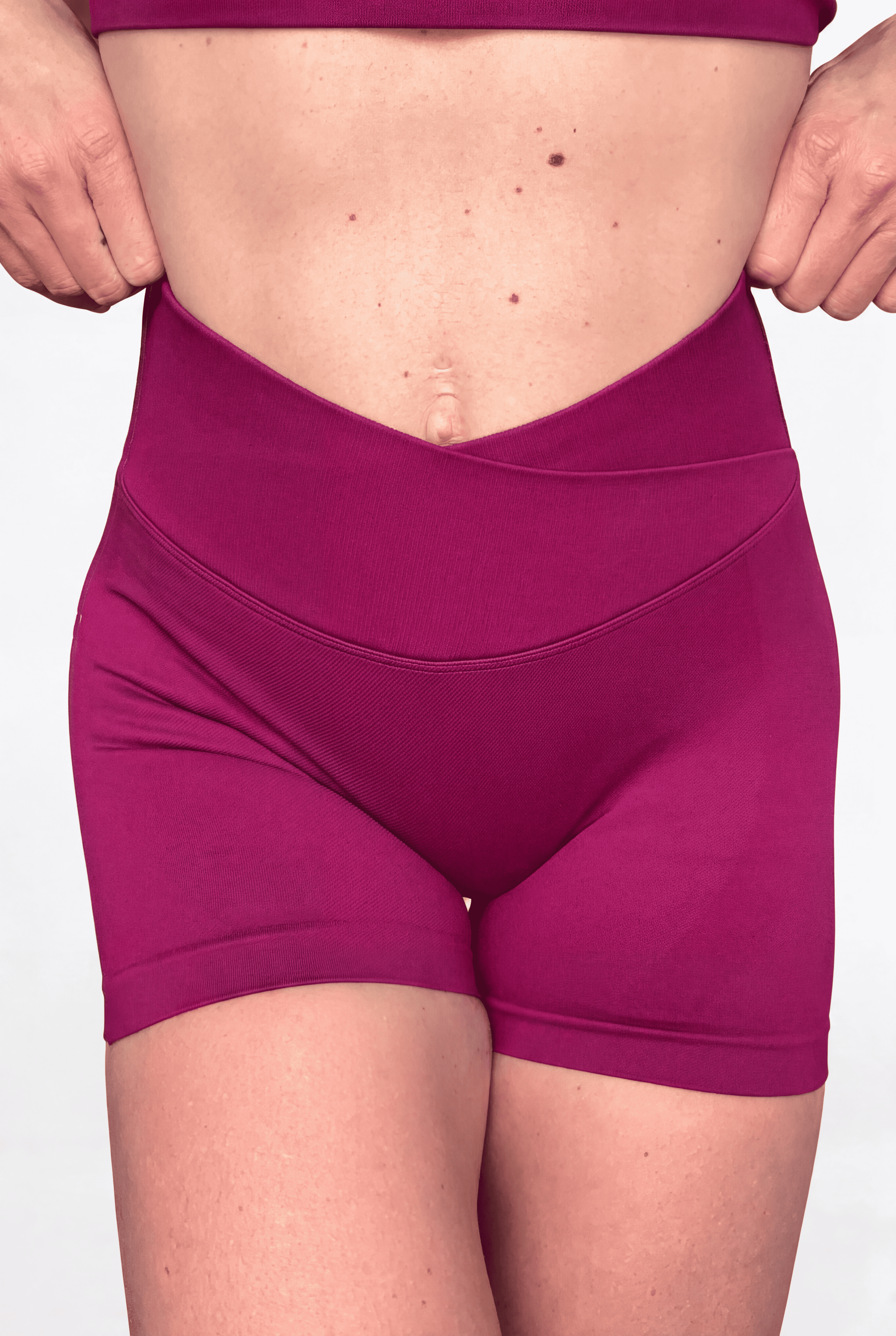A close-up of a model wearing high-waisted magenta athletic shorts, showing the V waistband and fit against a plain light background.