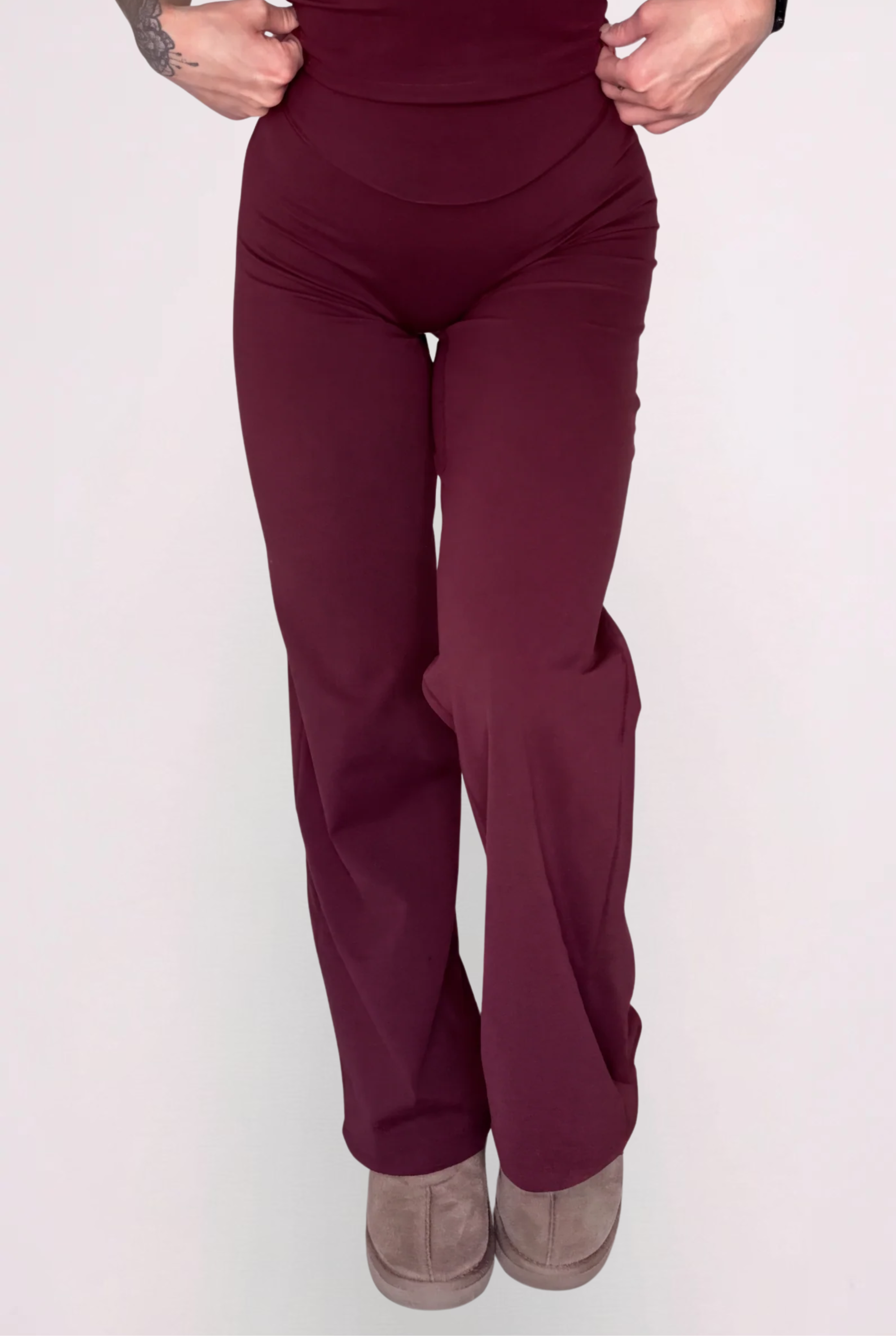 A model wearing a matching wine two-piece set consisting of a spaghetti-strap camisole top and high-waisted wide-leg pants, shown against a solid light grey background.