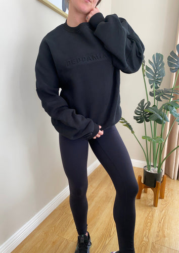 Crew neck jumper in black with fleece lined fabric, ribbed panel inserts, dropped shoulders and iconic embossed logo