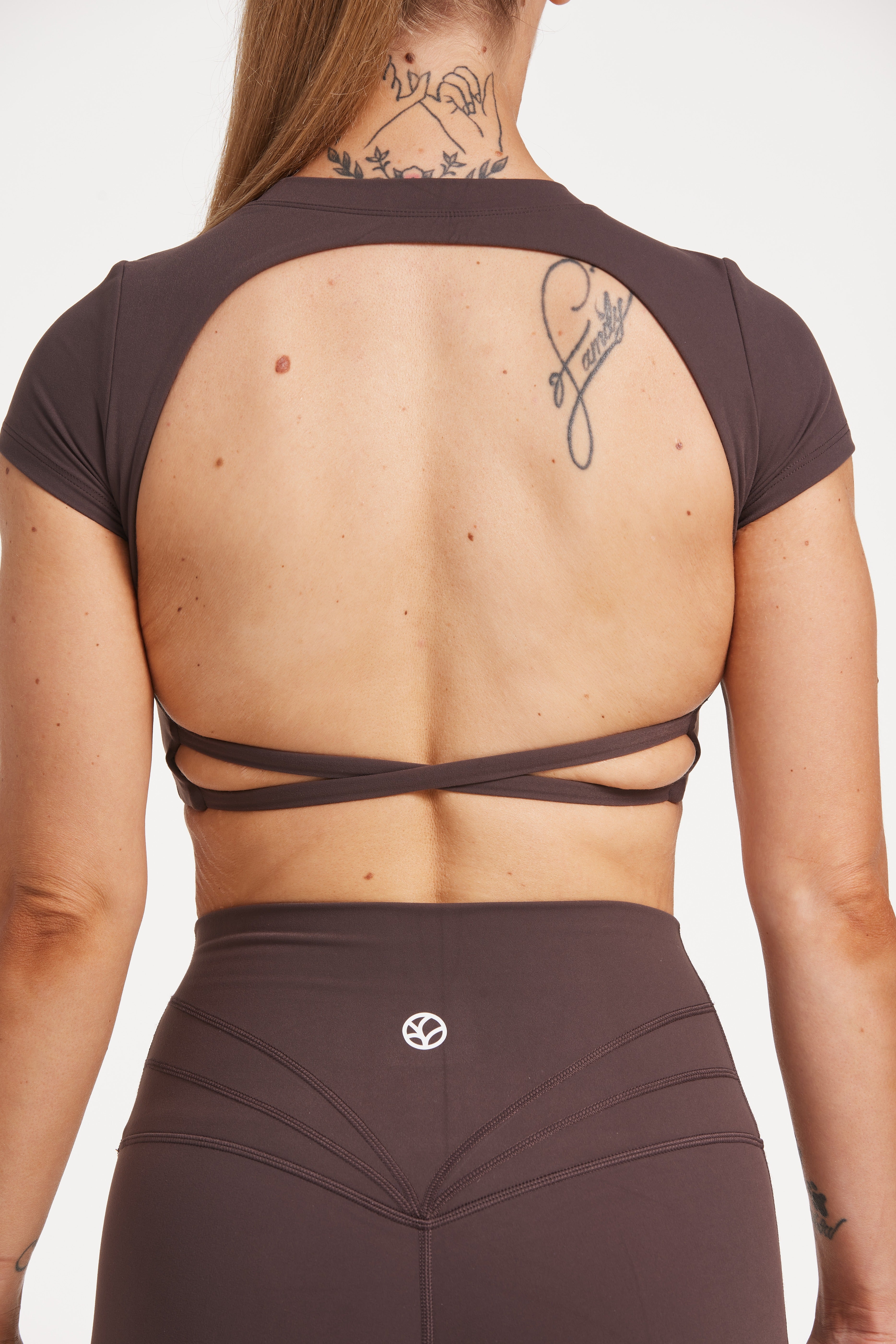 Buttery soft high waisted women's gym tights with curved hem stitched detailing for a butt shaping effect, and no front rise seam, paired with an open back women's crop t-shirt with a supportive elasticated hem and triple layered fabric with removable pads for extra support and aesthetic cross back straps in dark chocolate.