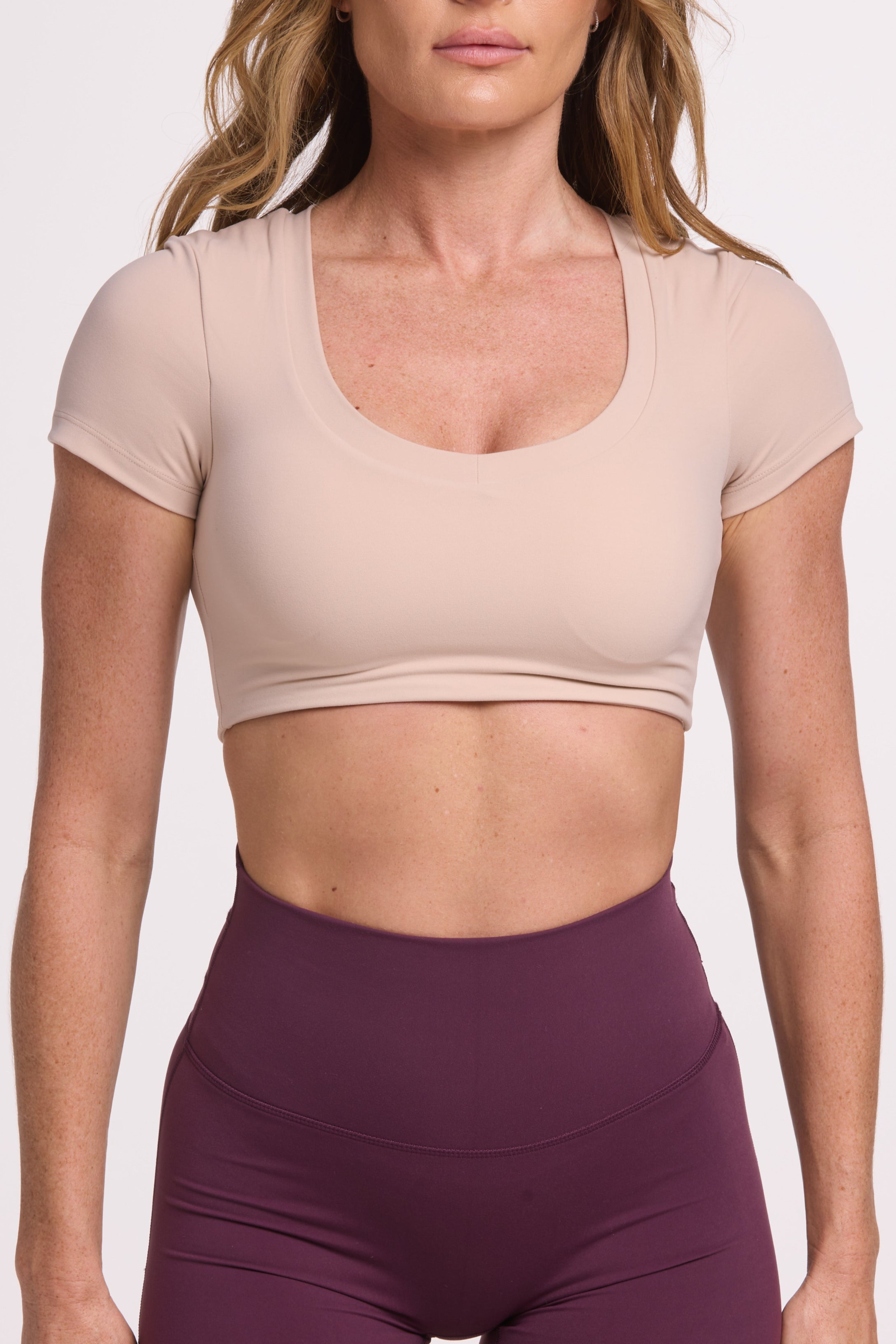 Buttery soft high waisted women's gym shorts with 4" inseam with curved stitched detailing for a butt shaping effect, and no front rise seam in mulberry wine paired with a V neck women's crop t-shirt with a supportive elasticated hem and triple layered fabric with removable pads for extra support in beige