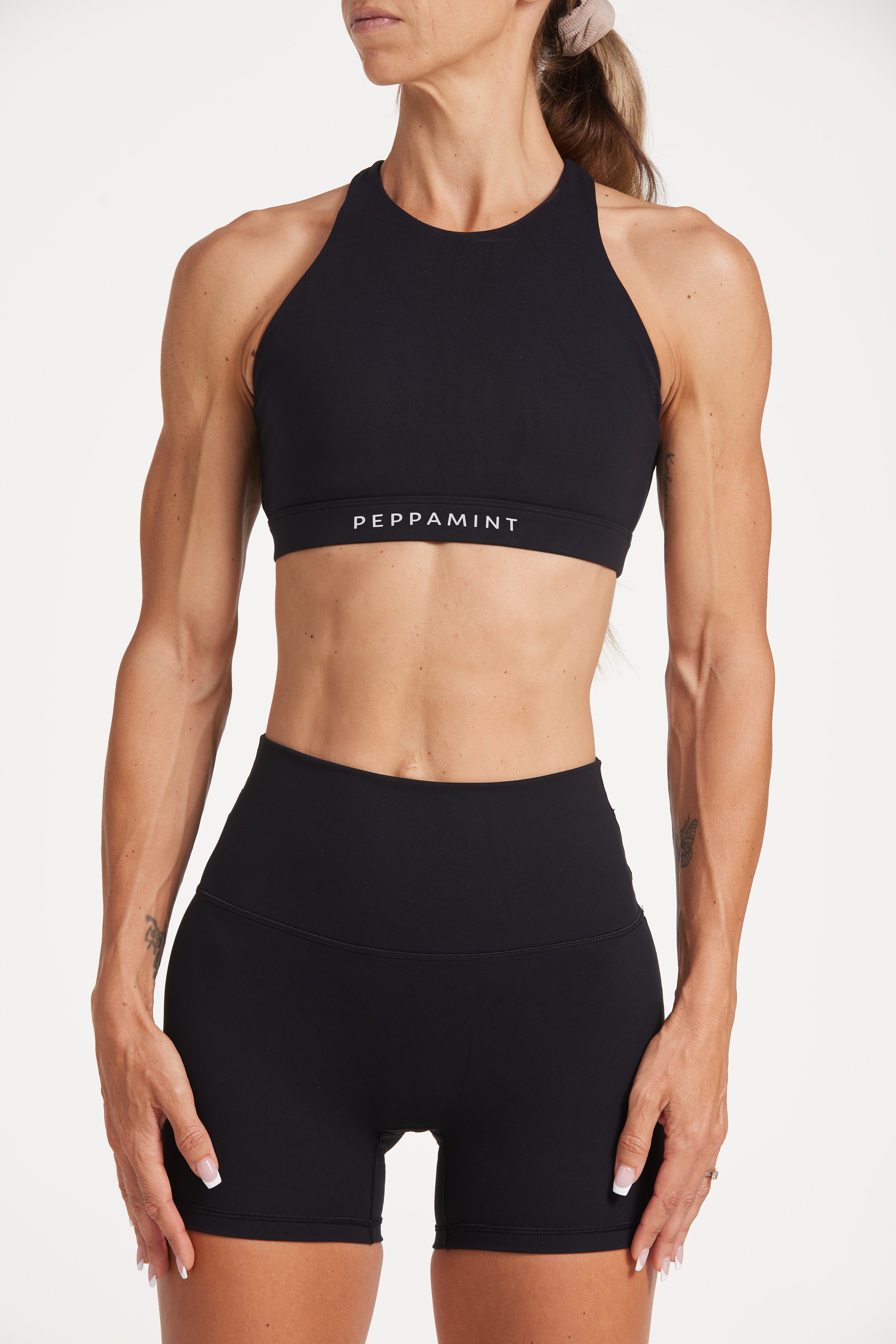 Buttery soft high waisted women's gym shorts with 4" inseam with curved stitched detailing for a butt shaping effect, and no front rise seam, paired with a high neck women's sports bra with a supportive elasticated hem and triple layered fabric with removable pads for extra support and crossover back straps in Black.