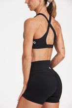 Load image into Gallery viewer, Buttery soft high waisted women&#39;s gym shorts with 4&quot; inseam with curved stitched detailing for a butt shaping effect, and no front rise seam, paired with a high neck women&#39;s sports bra with a supportive elasticated hem and triple layered fabric with removable pads for extra support and crossover back straps in Black.
