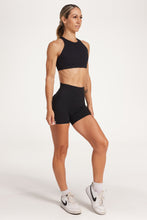 Load image into Gallery viewer, Buttery soft high waisted women&#39;s gym shorts with 4&quot; inseam with curved stitched detailing for a butt shaping effect, and no front rise seam, paired with a high neck women&#39;s sports bra with a supportive elasticated hem and triple layered fabric with removable pads for extra support and crossover back straps in Black.
