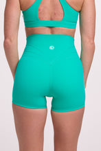 Load image into Gallery viewer, Buttery soft high waisted women&#39;s gym shorts with 4&quot; inseam with curved stitched detailing for a butt shaping effect, and no front rise seam, paired with a high neck women&#39;s sports bra with a supportive elasticated hem and triple layered fabric with removable pads for extra support and crossover back straps in cyan green
