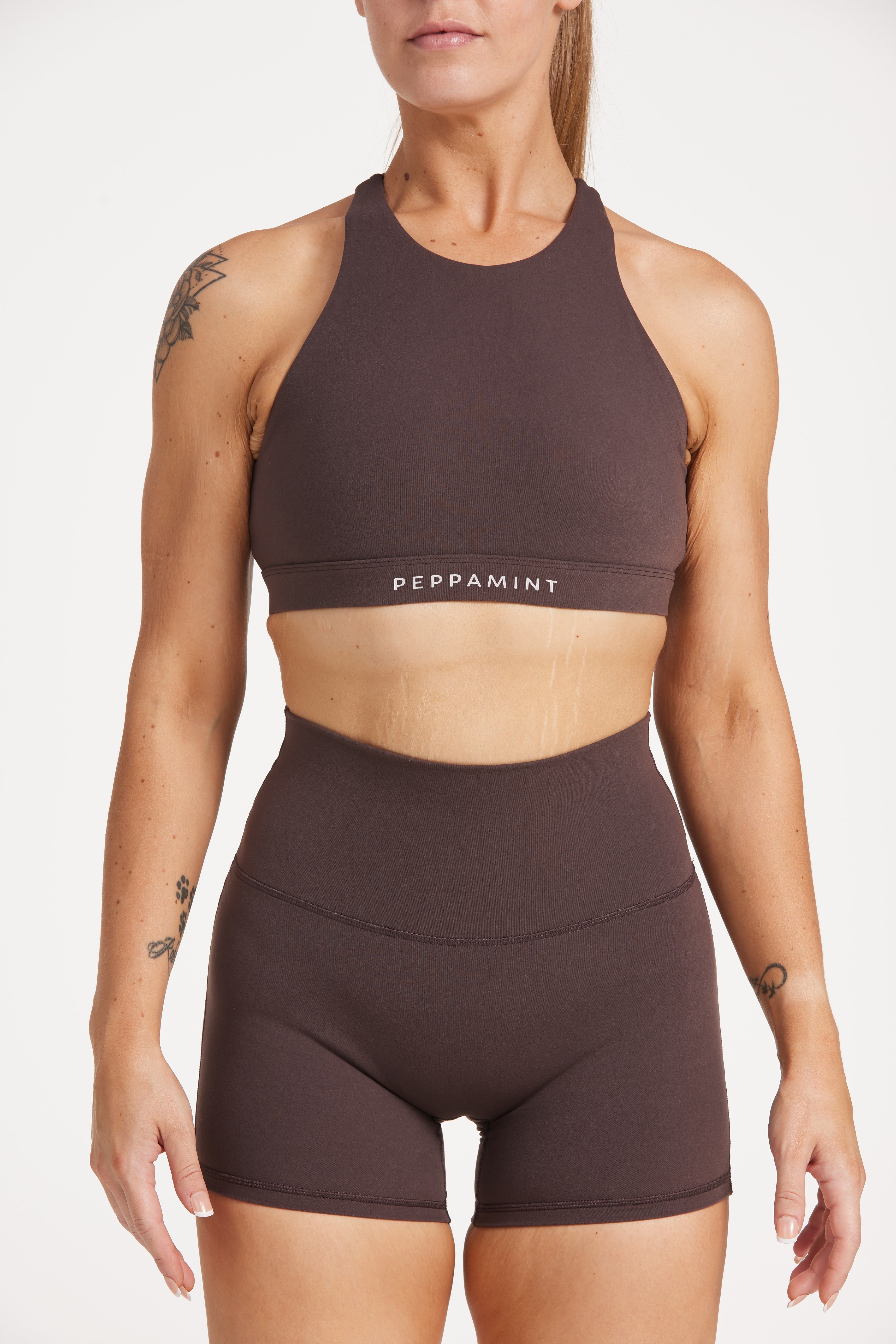 Buttery soft high waisted women's gym shorts with 4" inseam with curved stitched detailing for a butt shaping effect, and no front rise seam, paired with a high neck women's sports bra with a supportive elasticated hem and triple layered fabric with removable pads for extra support and crossover back straps in Dark Chocolate.