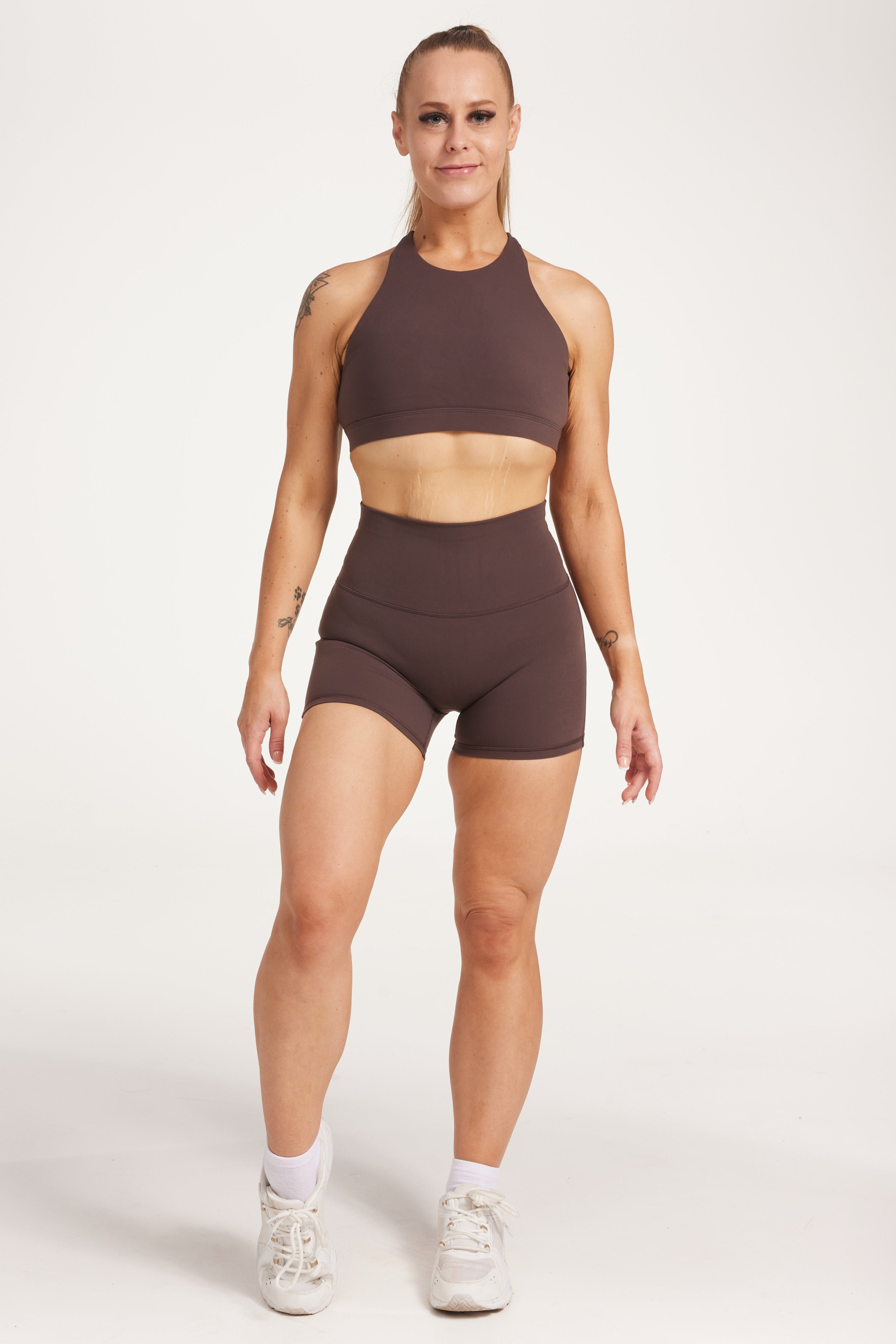Buttery soft high waisted women's gym shorts with 4" inseam with curved stitched detailing for a butt shaping effect, and no front rise seam, paired with a high neck women's sports bra with a supportive elasticated hem and triple layered fabric with removable pads for extra support and crossover back straps in Dark Chocolate.