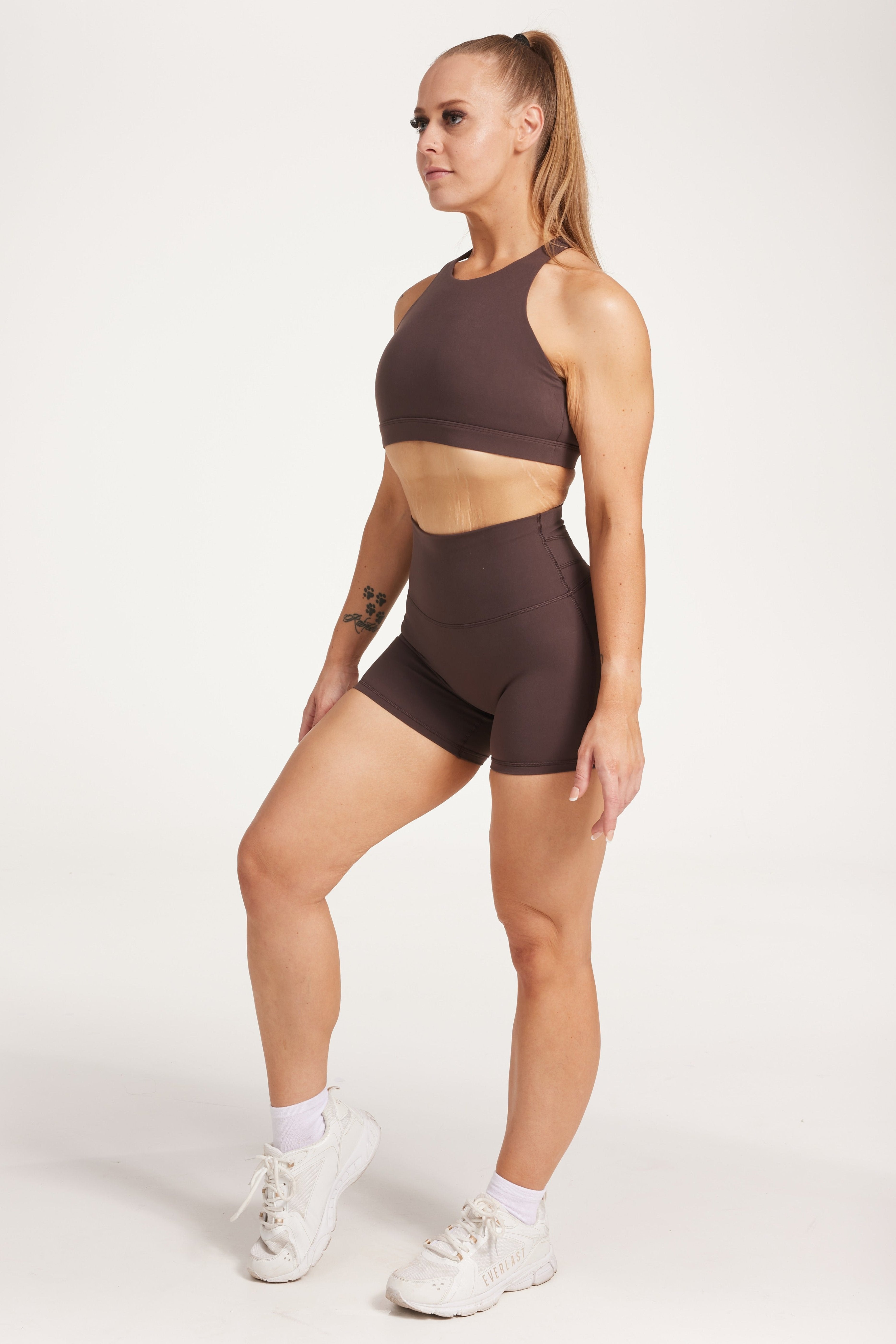 Buttery soft high waisted women's gym shorts with 4" inseam with curved stitched detailing for a butt shaping effect, and no front rise seam, paired with a high neck women's sports bra with a supportive elasticated hem and triple layered fabric with removable pads for extra support and crossover back straps in Dark Chocolate.