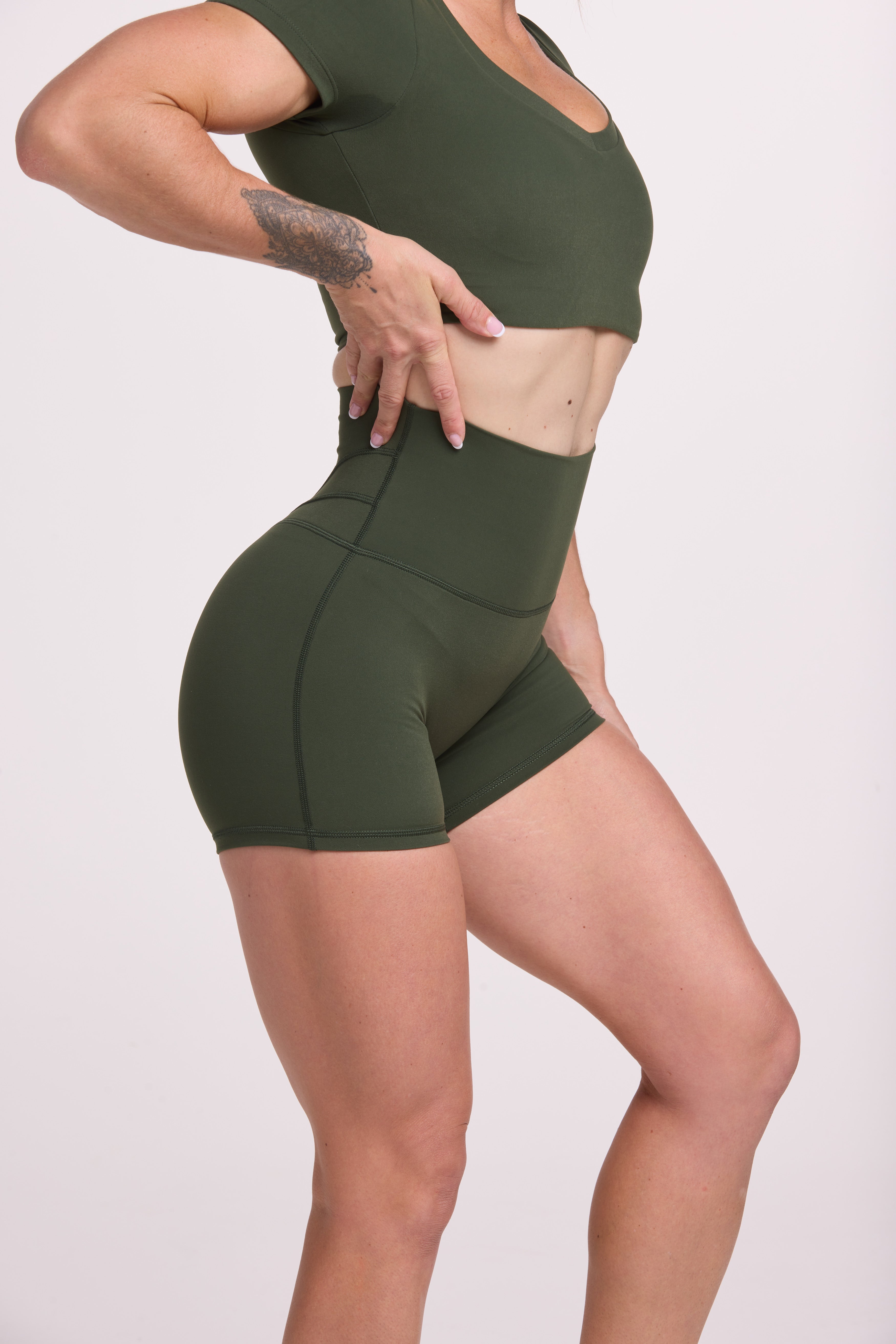 Buttery soft high waisted women's gym shorts with 4" inseam with curved stitched detailing for a butt shaping effect, and no front rise seam, paired with a V neck women's crop t-shirt with a supportive elasticated hem and triple layered fabric with removable pads for extra support in forest green