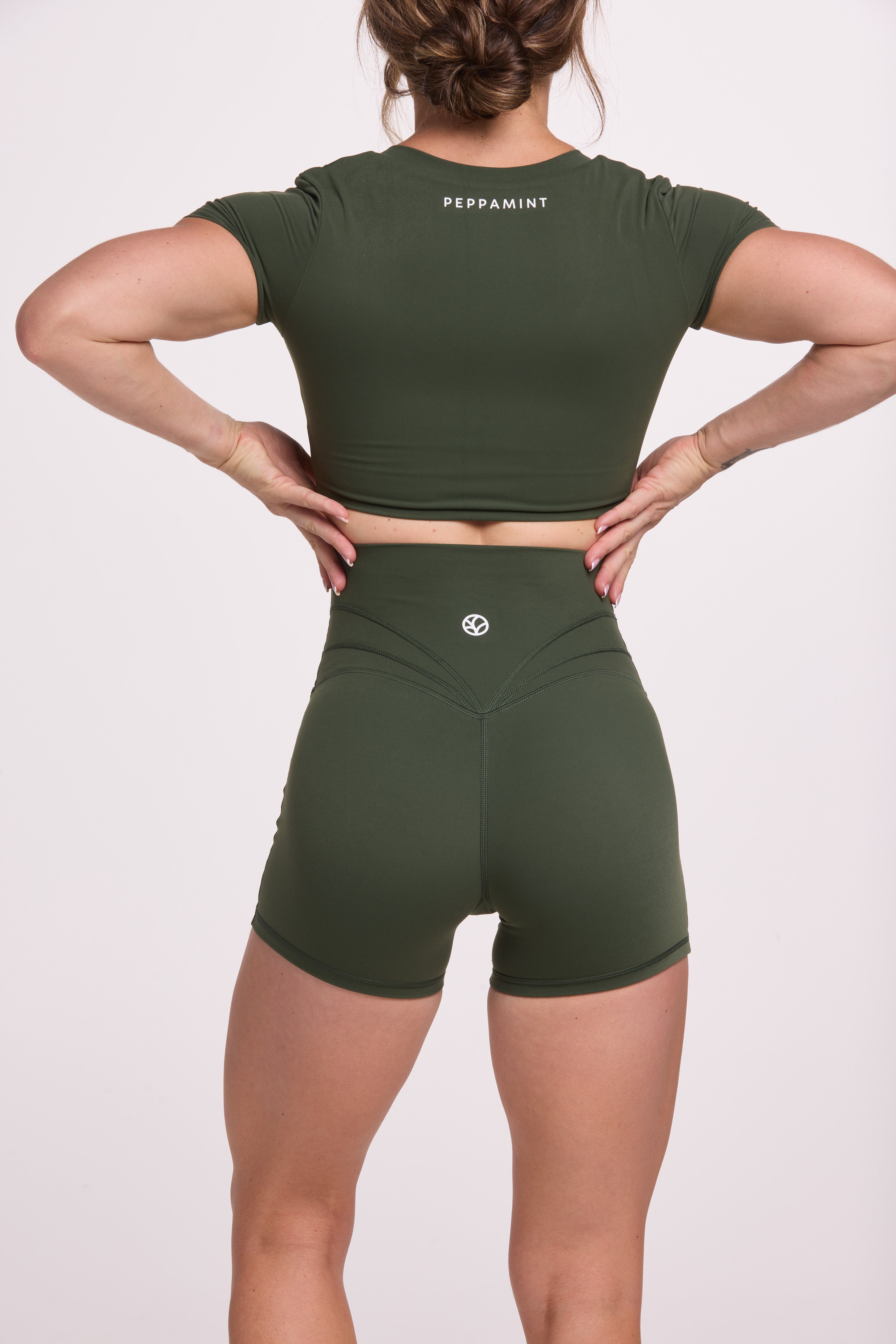 Buttery soft high waisted women's gym shorts with 4" inseam with curved stitched detailing for a butt shaping effect, and no front rise seam, paired with a V neck women's crop t-shirt with a supportive elasticated hem and triple layered fabric with removable pads for extra support in forest green