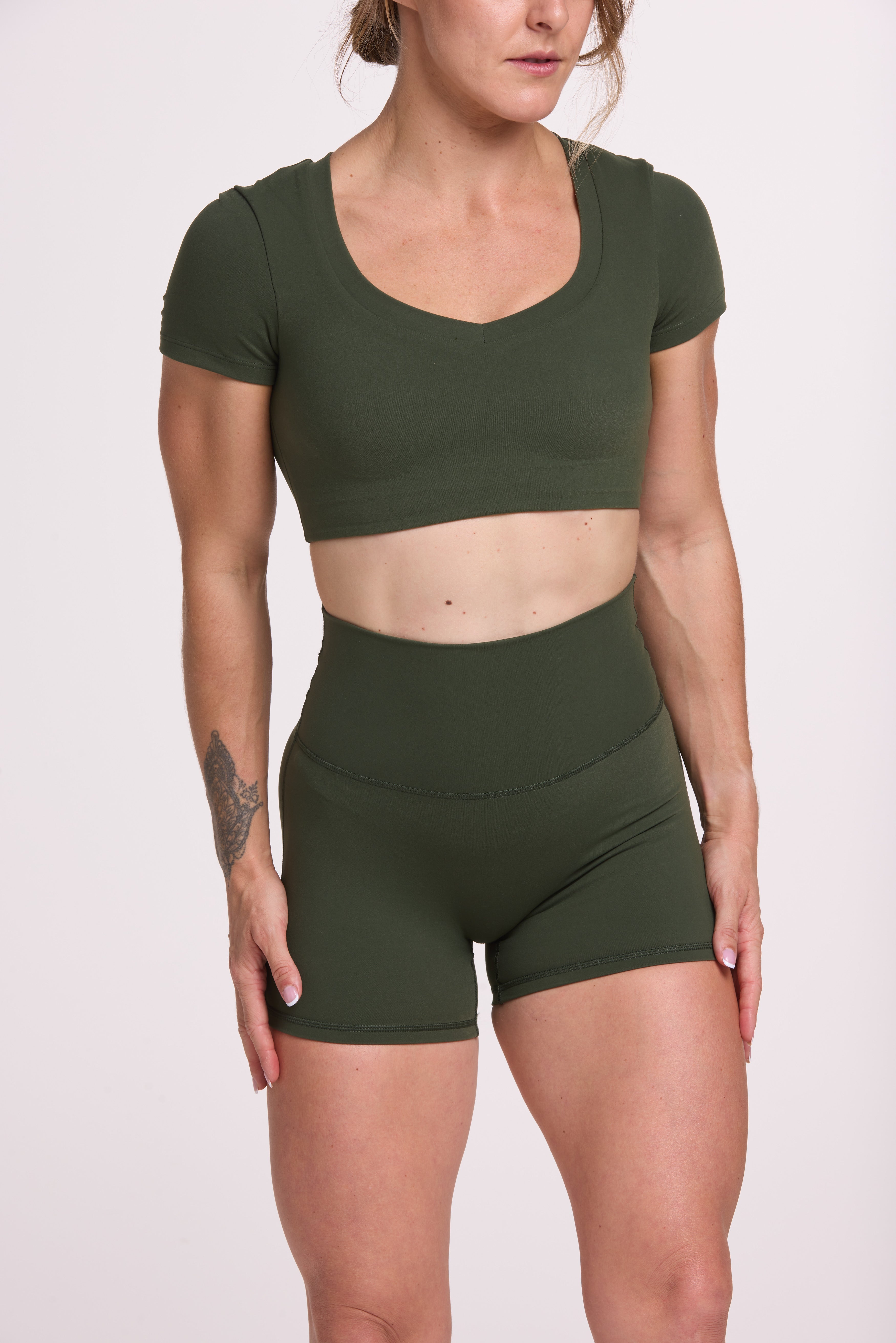 Buttery soft high waisted women's gym shorts with 4" inseam with curved stitched detailing for a butt shaping effect, and no front rise seam, paired with a V neck women's crop t-shirt with a supportive elasticated hem and triple layered fabric with removable pads for extra support in forest green