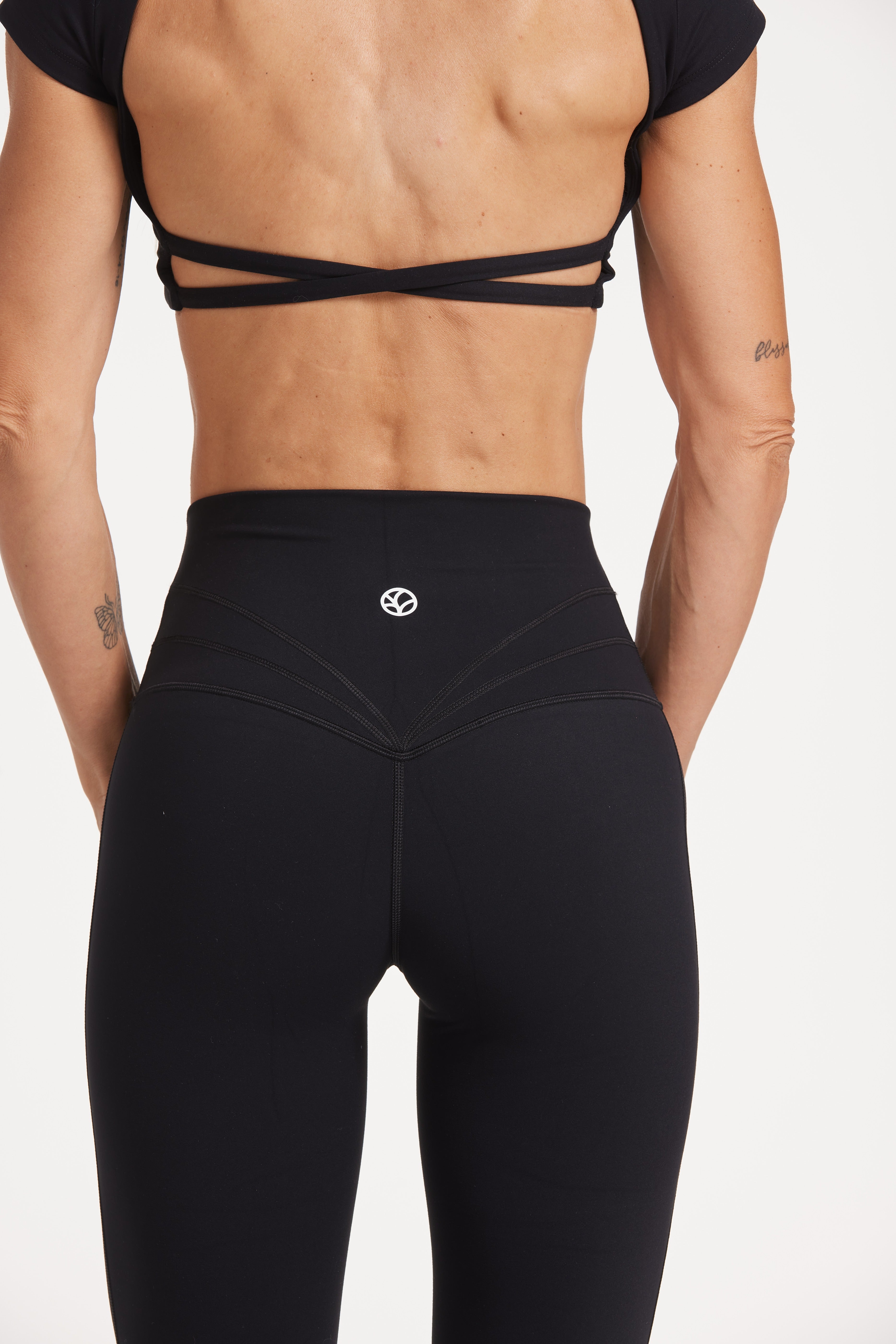 Buttery soft high waisted women's gym tights with curved hem stitched detailing for a butt shaping effect, and no front rise seam, paired with an open back women's crop t-shirt with a supportive elasticated hem and triple layered fabric with removable pads for extra support and aesthetic cross back straps in Black.
