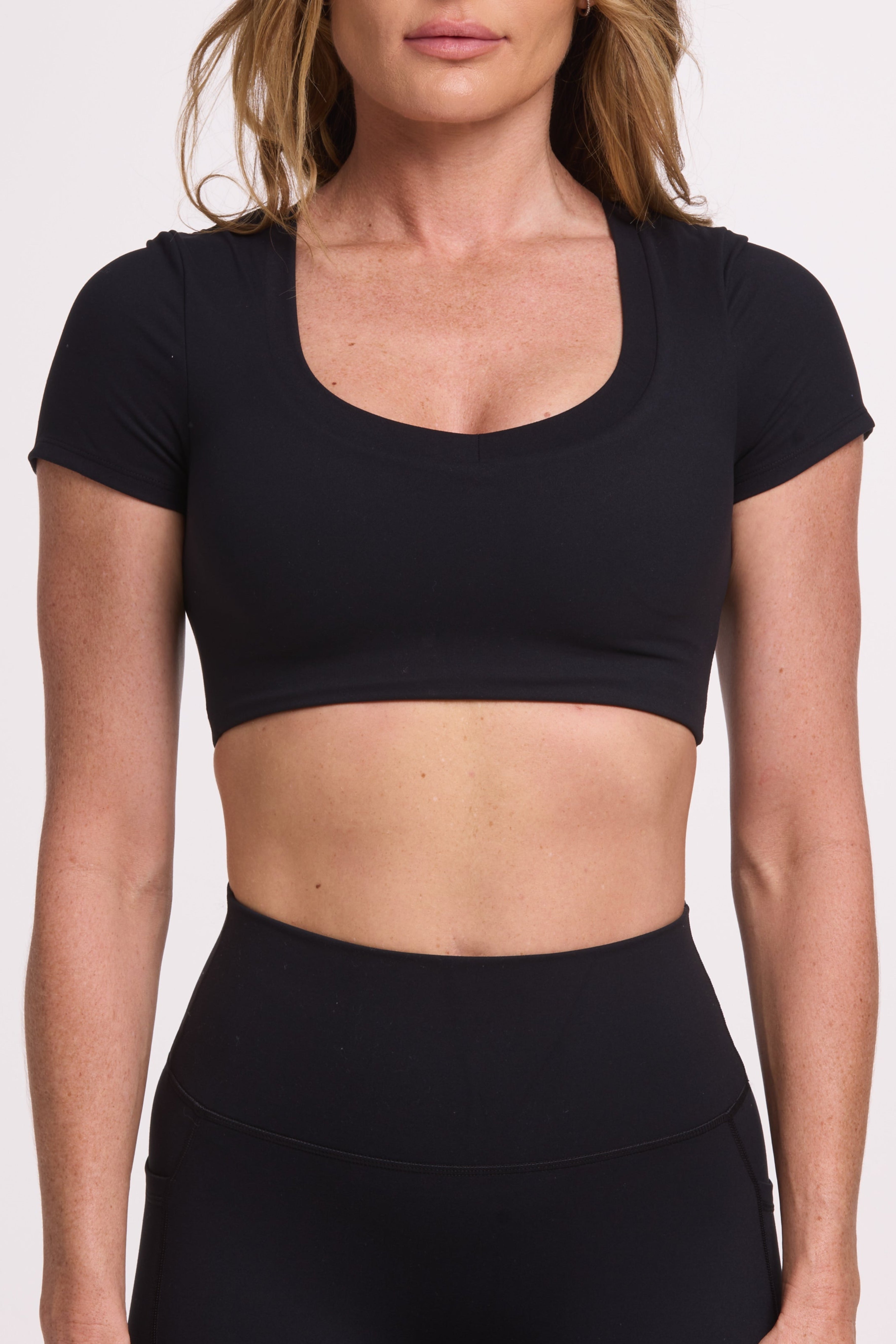 Buttery soft high waisted women's gym tights with practical pockets, sweetheart back seams for an upper glute shaping effect, and no front rise seam, paired with an V neck women's crop t-shirt with a supportive elasticated hem and triple layered fabric with removable pads for extra support in black