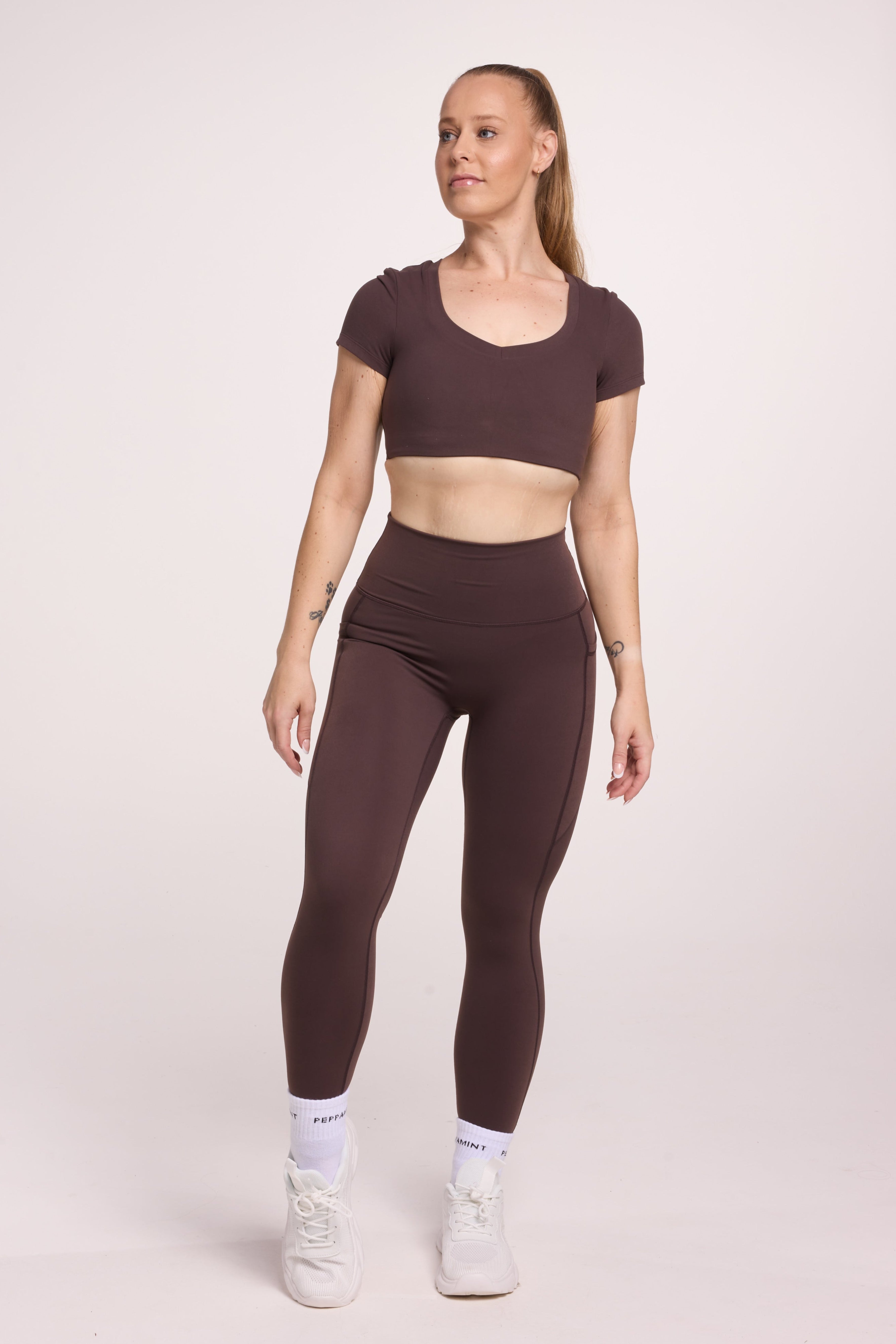 Buttery soft high waisted women's gym tights with practical pockets, sweetheart back seams for an upper glute shaping effect, and no front rise seam, paired with an V neck women's crop t-shirt with a supportive elasticated hem and triple layered fabric with removable pads for extra support in chocolate
