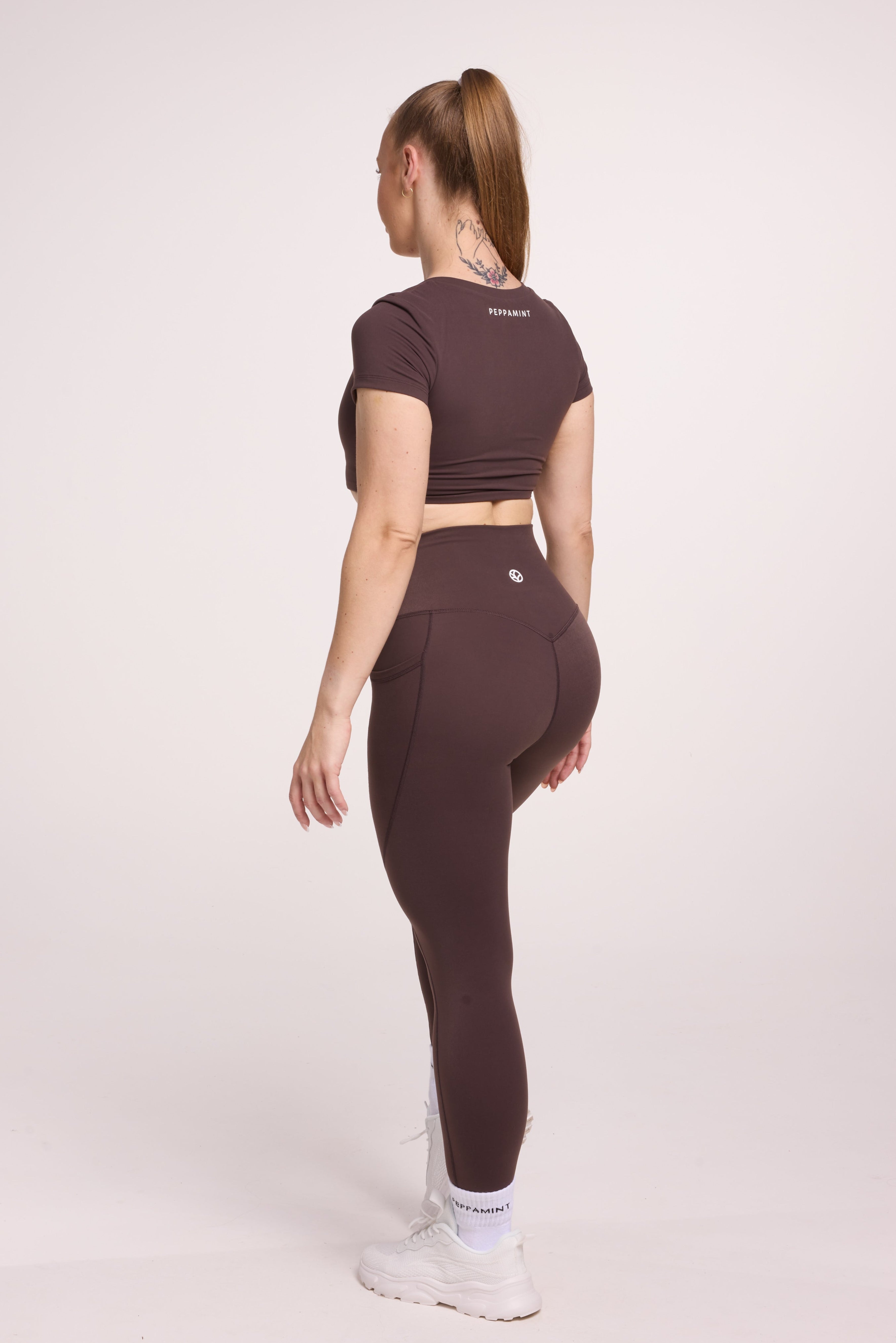 Buttery soft high waisted women's gym tights with practical pockets, sweetheart back seams for an upper glute shaping effect, and no front rise seam, paired with an V neck women's crop t-shirt with a supportive elasticated hem and triple layered fabric with removable pads for extra support in chocolate