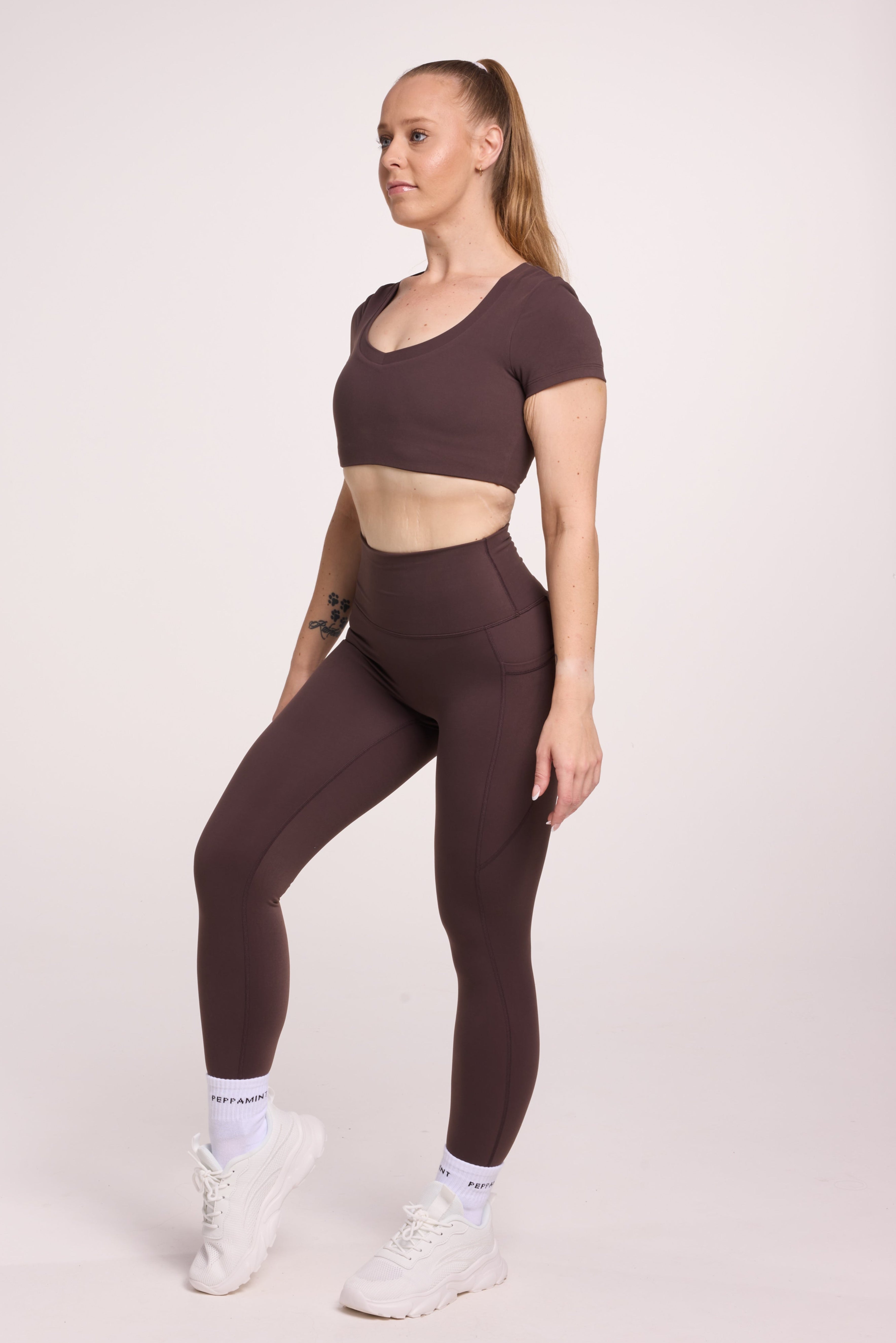 Buttery soft high waisted women's gym tights with practical pockets, sweetheart back seams for an upper glute shaping effect, and no front rise seam, paired with an V neck women's crop t-shirt with a supportive elasticated hem and triple layered fabric with removable pads for extra support in chocolate