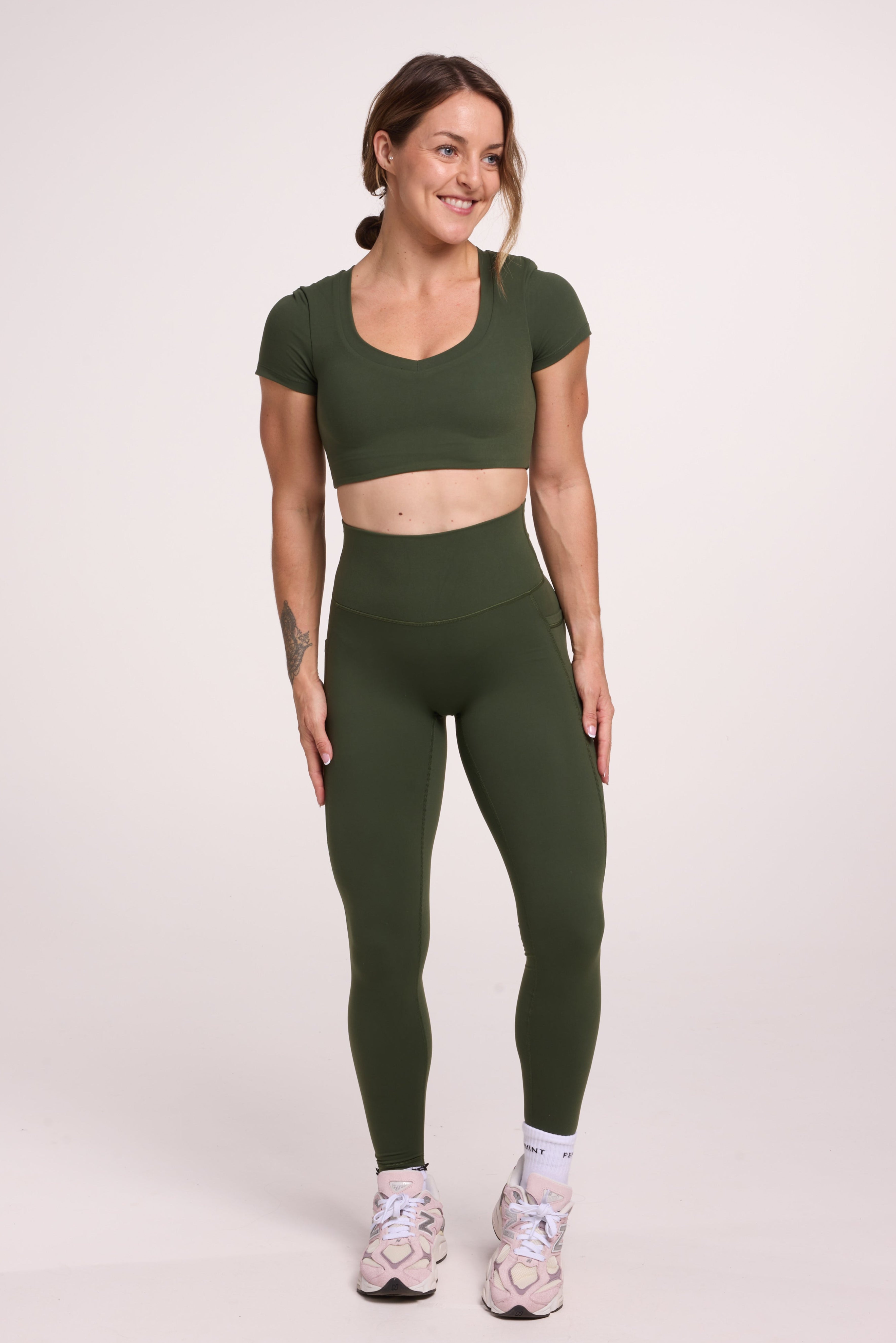 Buttery soft high waisted women's gym tights with practical pockets, sweetheart back seams for an upper glute shaping effect, and no front rise seam, paired with an V neck women's crop t-shirt with a supportive elasticated hem and triple layered fabric with removable pads for extra support in forest green