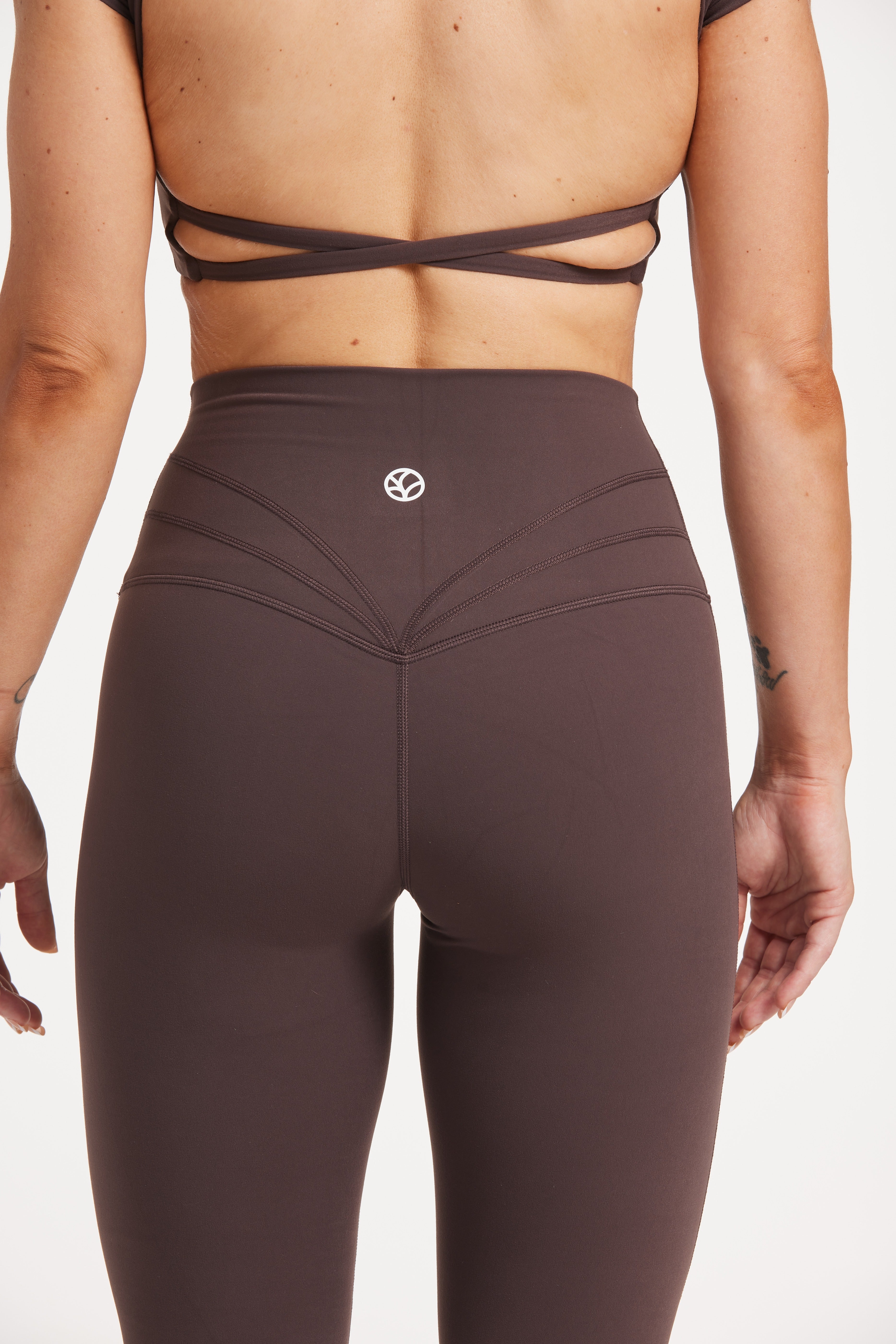Buttery soft high waisted women's gym tights with curved hem stitched detailing for a butt shaping effect, and no front rise seam, paired with an open back women's crop t-shirt with a supportive elasticated hem and triple layered fabric with removable pads for extra support and aesthetic cross back straps in dark chocolate.