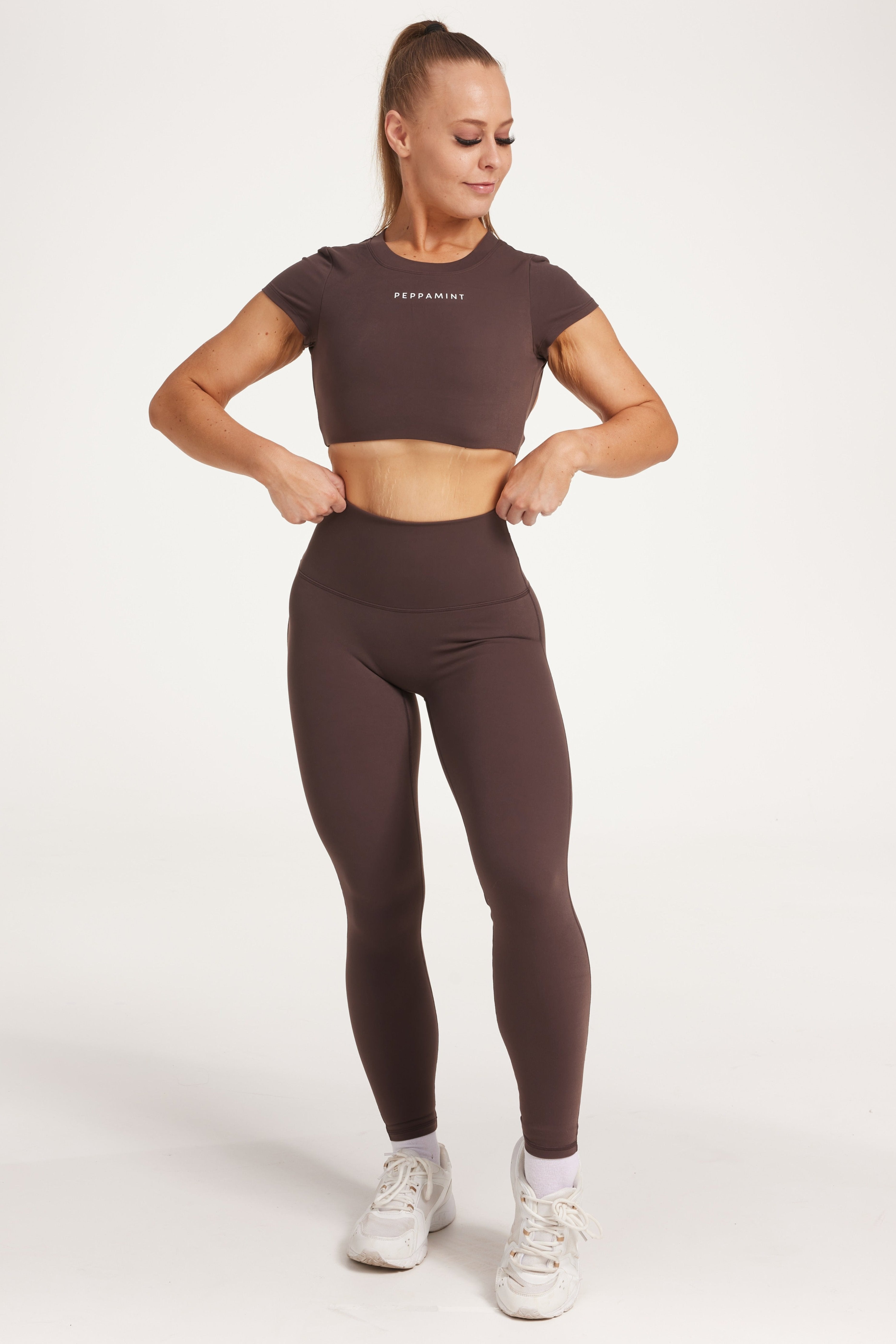 Buttery soft high waisted women's gym tights with curved hem stitched detailing for a butt shaping effect, and no front rise seam, paired with an open back women's crop t-shirt with a supportive elasticated hem and triple layered fabric with removable pads for extra support and aesthetic cross back straps in dark chocolate.
