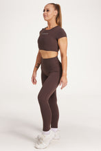 Load image into Gallery viewer, Buttery soft high waisted women&#39;s gym tights with curved hem stitched detailing for a butt shaping effect, and no front rise seam, paired with an open back women&#39;s crop t-shirt with a supportive elasticated hem and triple layered fabric with removable pads for extra support and aesthetic cross back straps in dark chocolate.
