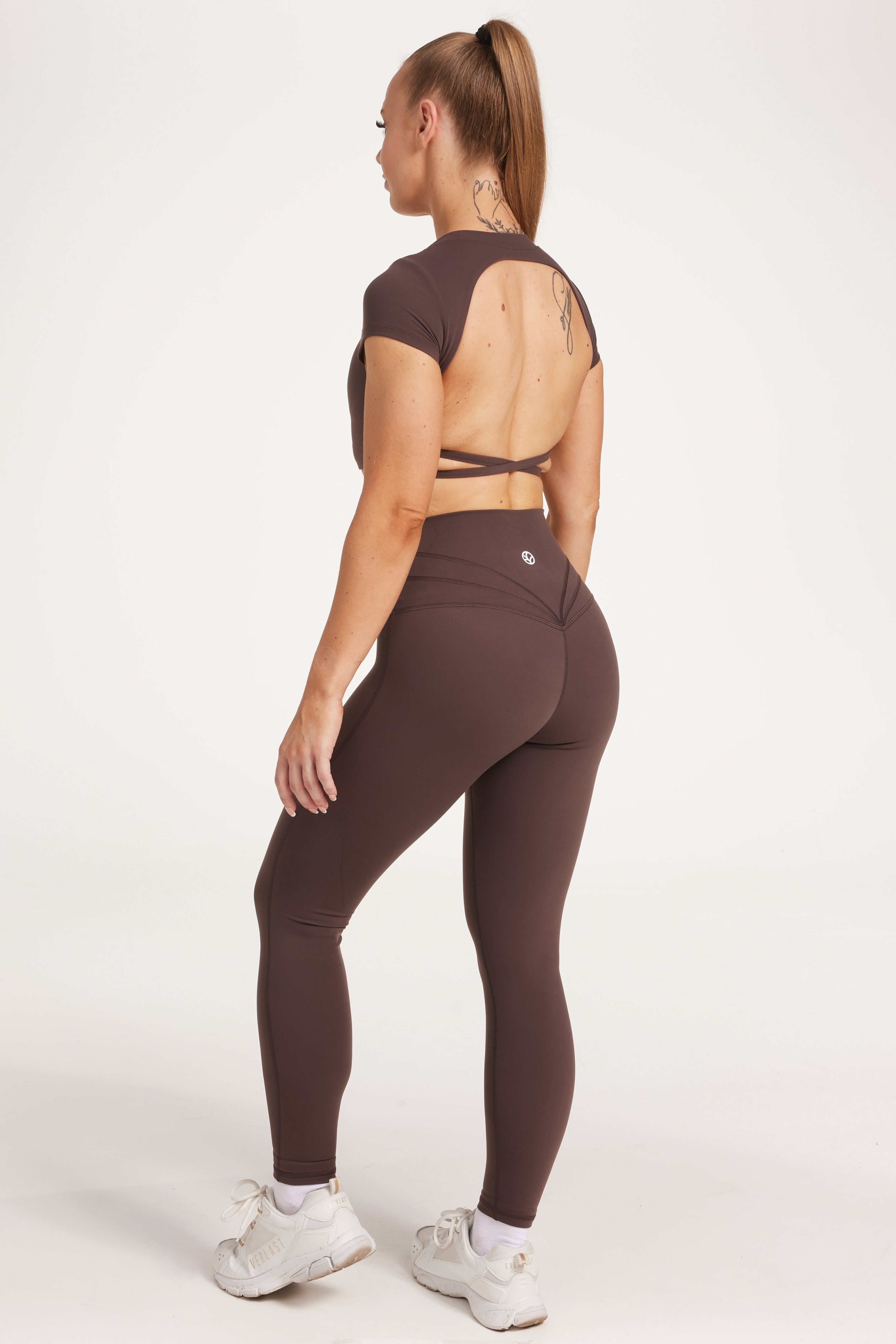 Buttery soft high waisted women's gym tights with curved hem stitched detailing for a butt shaping effect, and no front rise seam, paired with an open back women's crop t-shirt with a supportive elasticated hem and triple layered fabric with removable pads for extra support and aesthetic cross back straps in dark chocolate.