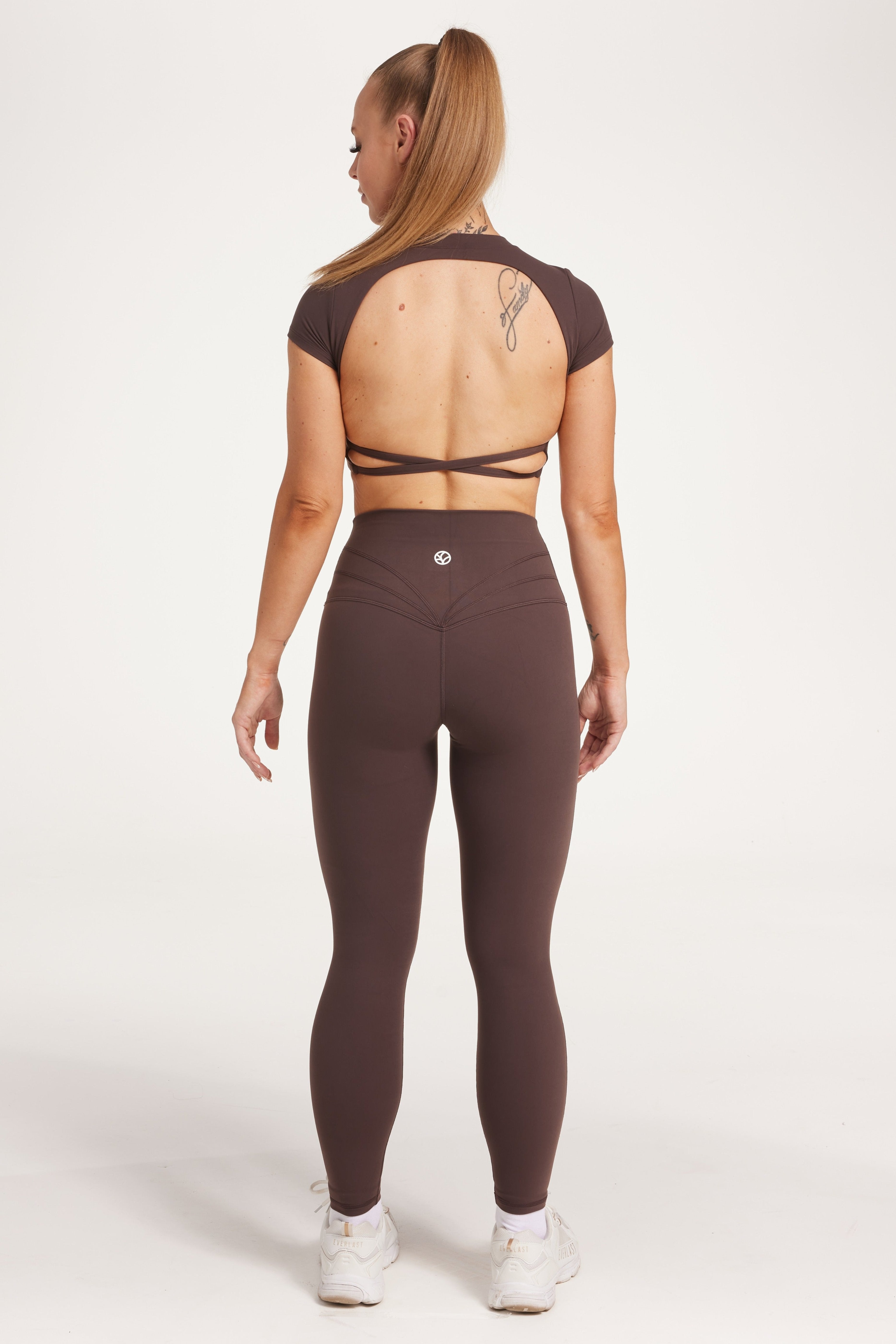Buttery soft high waisted women's gym tights with curved hem stitched detailing for a butt shaping effect, and no front rise seam, paired with an open back women's crop t-shirt with a supportive elasticated hem and triple layered fabric with removable pads for extra support and aesthetic cross back straps in dark chocolate.