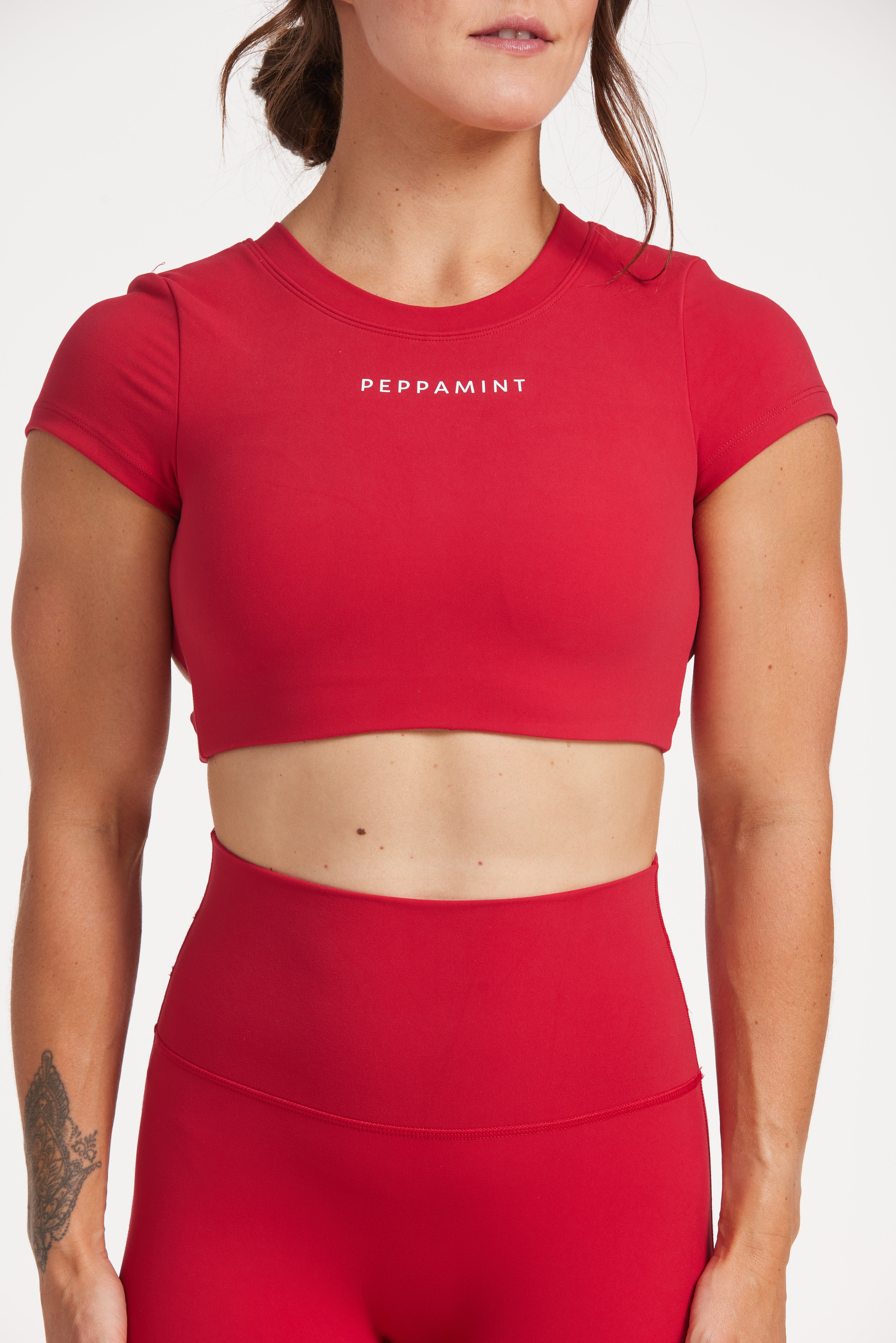 Buttery soft high waisted women's gym tights with curved hem stitched detailing for a butt shaping effect, and no front rise seam, paired with an open back women's crop t-shirt with a supportive elasticated hem and triple layered fabric with removable pads for extra support and aesthetic cross back straps in Raspberry red.