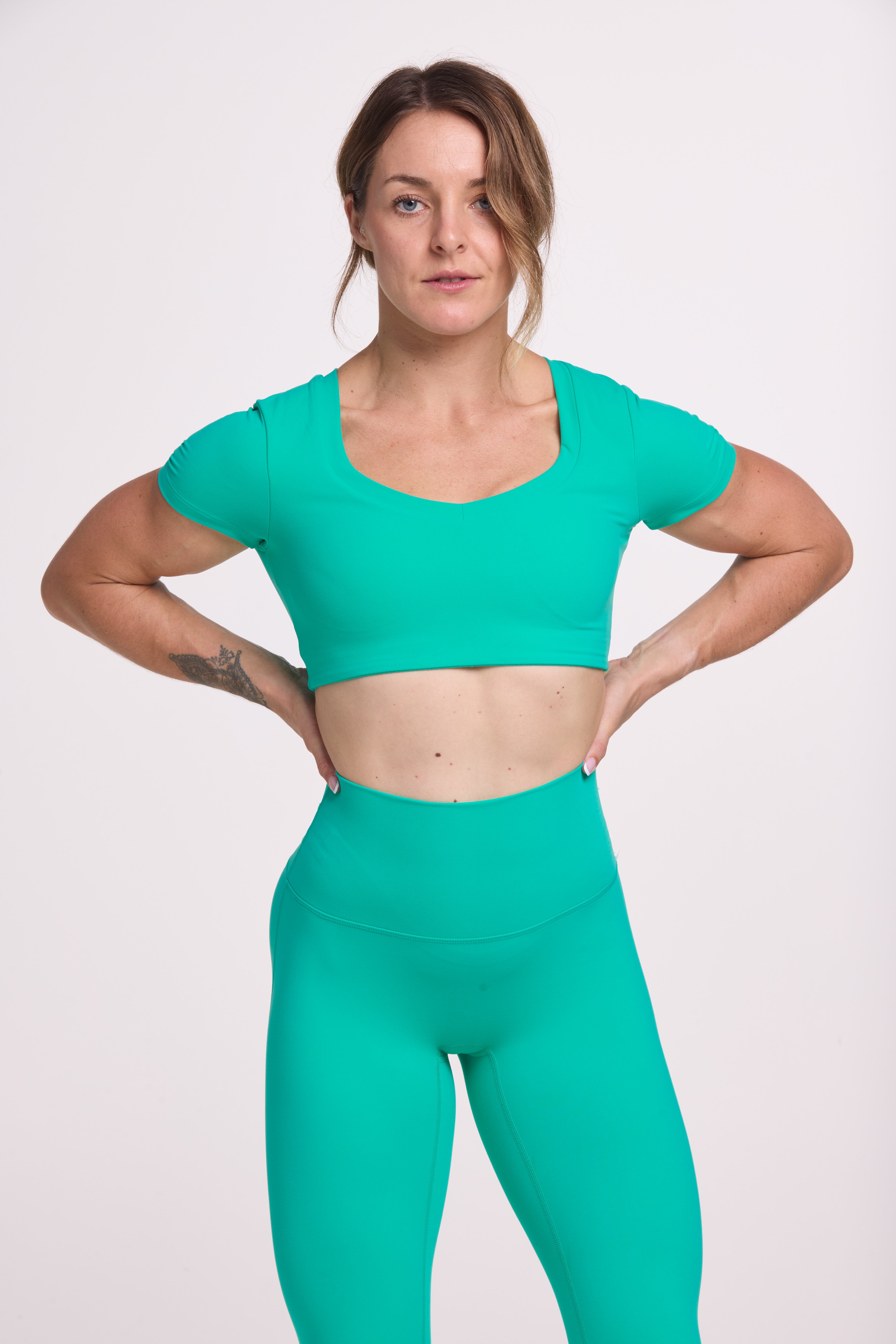 Buttery soft high waisted women's gym tights with curved back seam stitched detailing for a butt shaping effect, and no front rise seam paired with an V neck women's crop t-shirt with a supportive elasticated hem and triple layered fabric with removable pads for extra support in cyan green