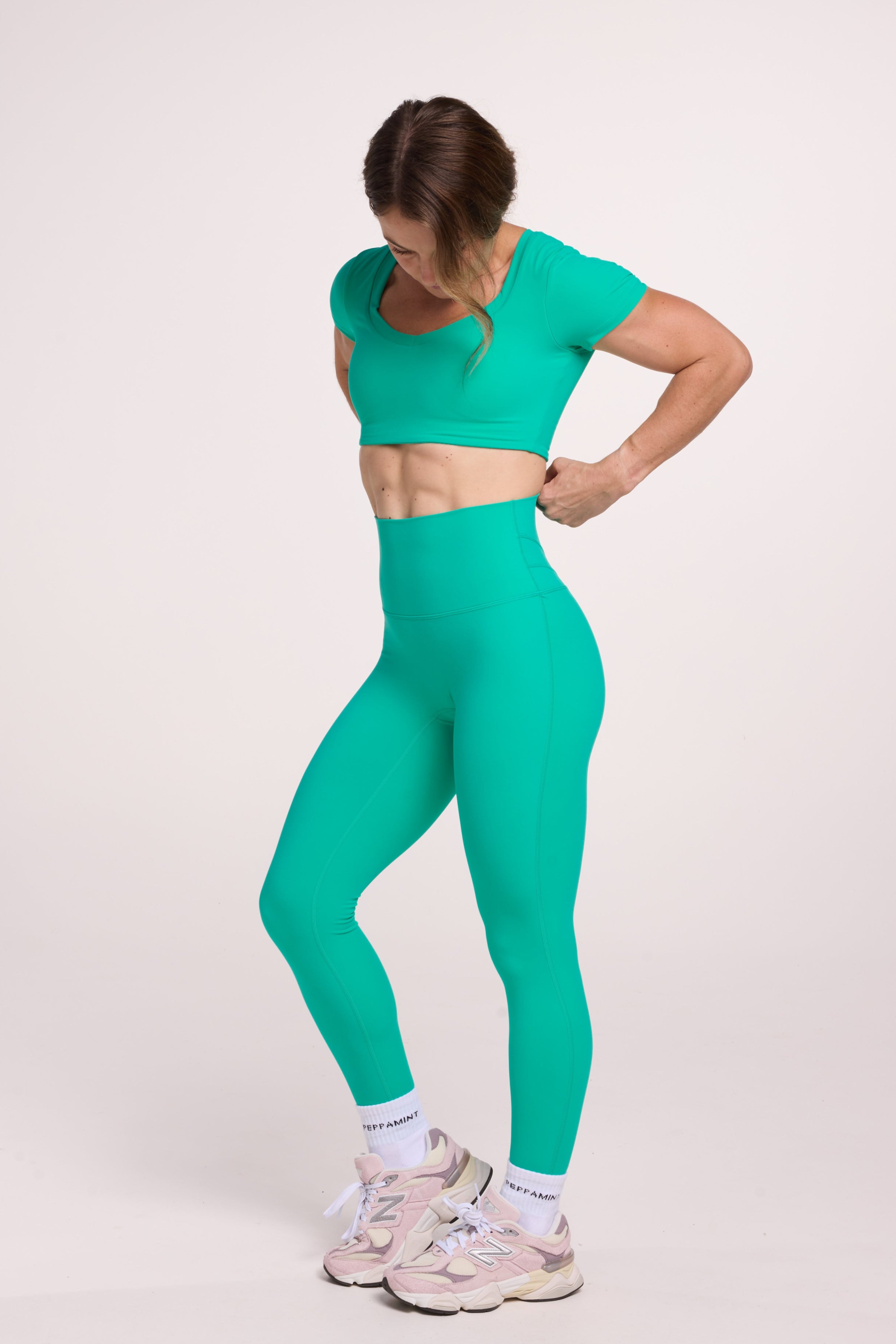 Buttery soft high waisted women's gym tights with curved back seam stitched detailing for a butt shaping effect, and no front rise seam paired with an V neck women's crop t-shirt with a supportive elasticated hem and triple layered fabric with removable pads for extra support in cyan green