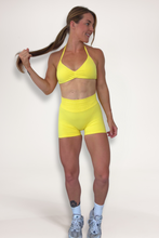 Load image into Gallery viewer, Seamless shorts with booty contouring panels, glute shaping seams, a thick supportive waistband paired with a minimalistic bra with sleek back straps and halter neck design for showcasing the back gains in buttercup yellow
