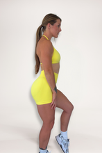 Load image into Gallery viewer, Seamless shorts with booty contouring panels, glute shaping seams, a thick supportive waistband paired with a minimalistic bra with sleek back straps and halter neck design for showcasing the back gains in buttercup yellow
