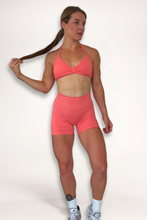 Load image into Gallery viewer, Seamless shorts with booty contouring panels, glute shaping seams, a thick supportive waistband paired with a minimalistic bra with sleek back straps and halter neck design for showcasing the back gains in coral
