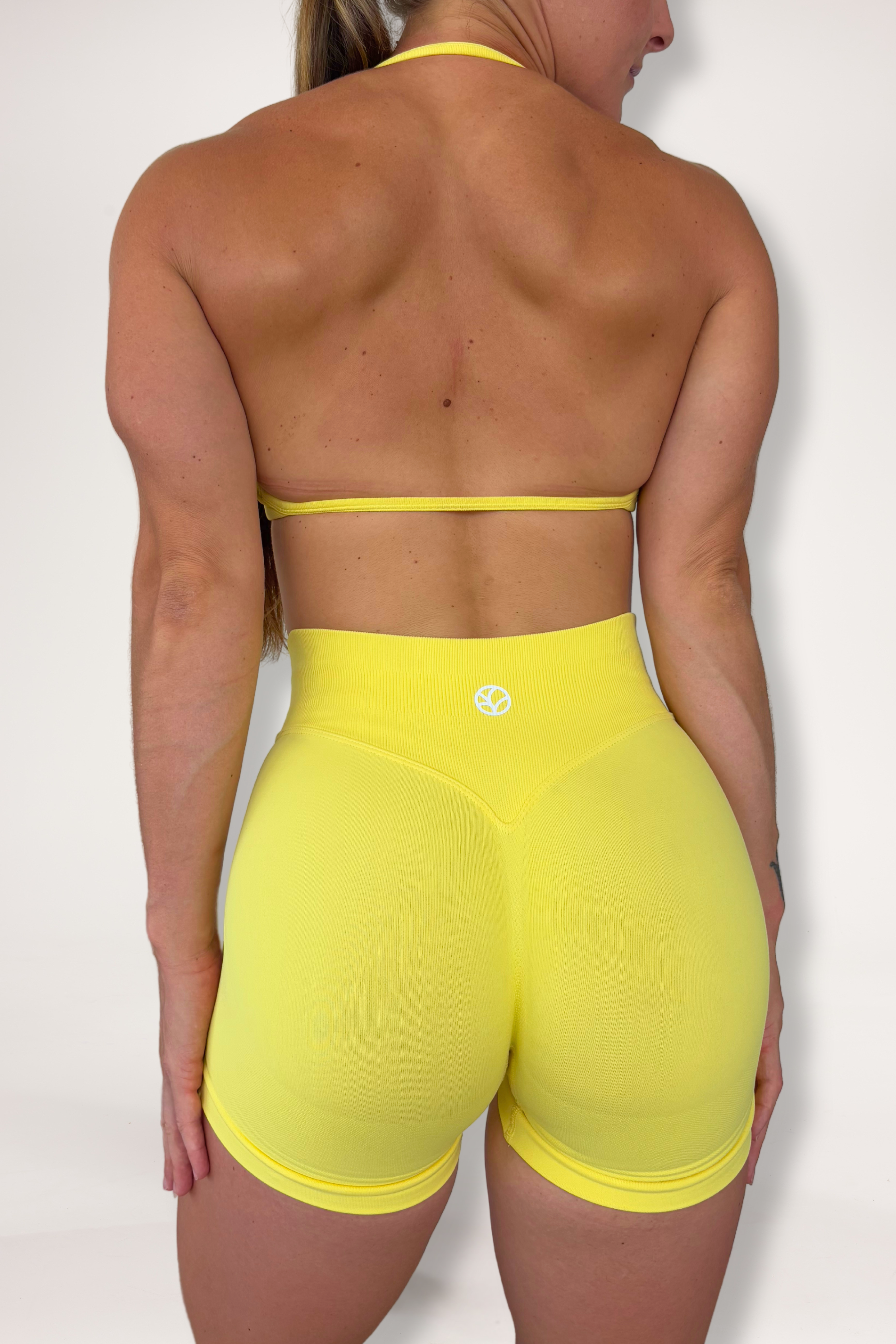 Seamless shorts with booty contouring panels, glute shaping seams, a thick supportive waistband paired with a minimalistic bra with sleek back straps and halter neck design for showcasing the back gains in buttercup yellow
