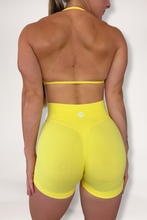 Load image into Gallery viewer, Seamless shorts with booty contouring panels, glute shaping seams, a thick supportive waistband paired with a minimalistic bra with sleek back straps and halter neck design for showcasing the back gains in buttercup yellow
