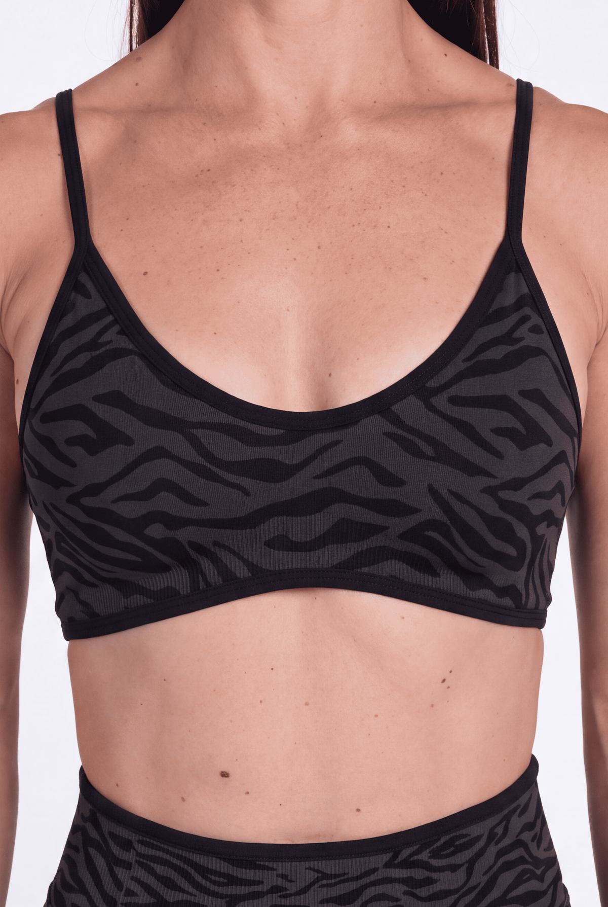 A woman wearing a black subtle tonal zebra print sports bra with black trim shown against a plain white studio background.