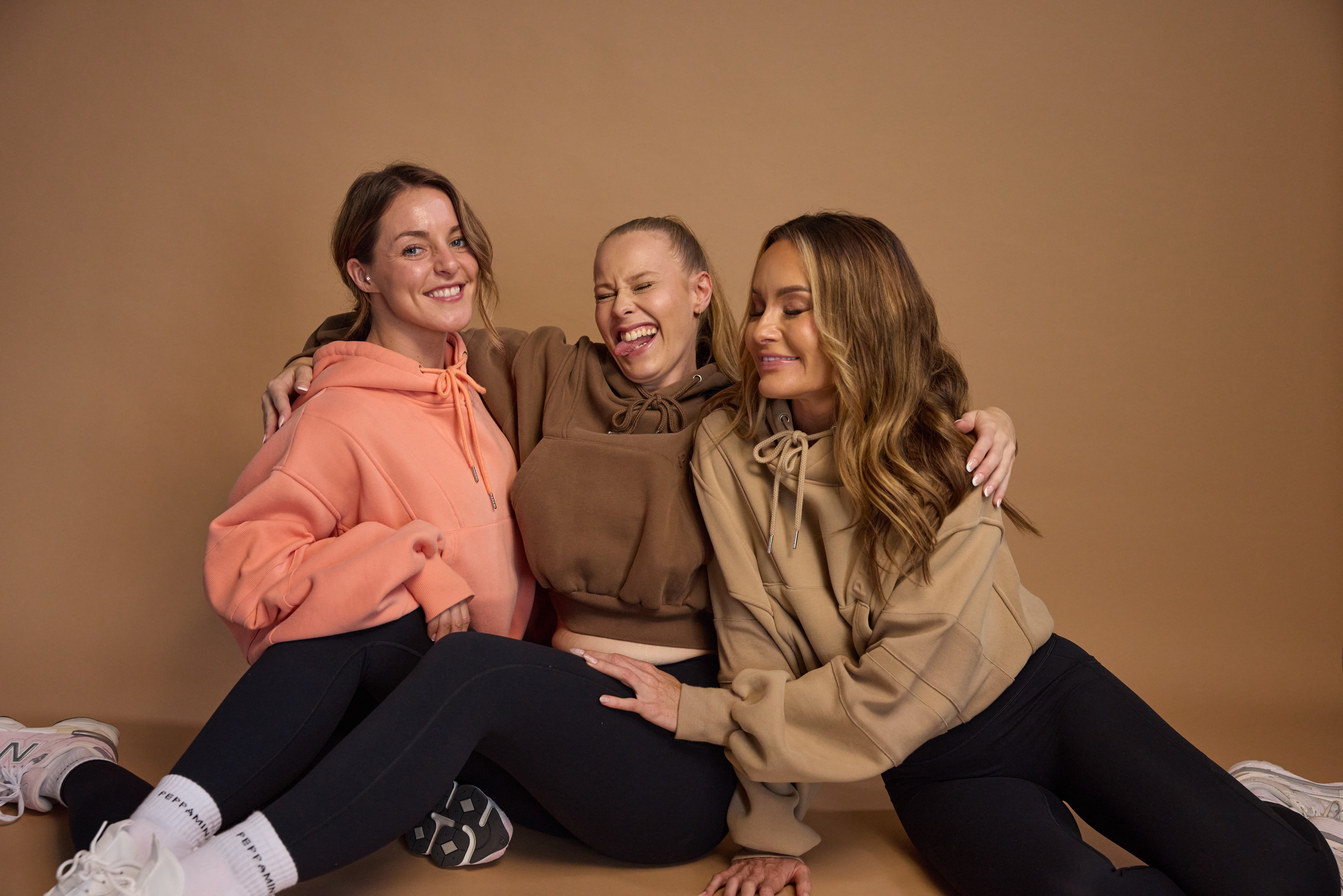 Oversize batwing hoodie, hip length, with slouchy oversized sleeves, piped seams, iconic ribbed panels and a kangaroo pocket with a hidden phone pocket inside in chocolate brown, coral and a beige sand colour