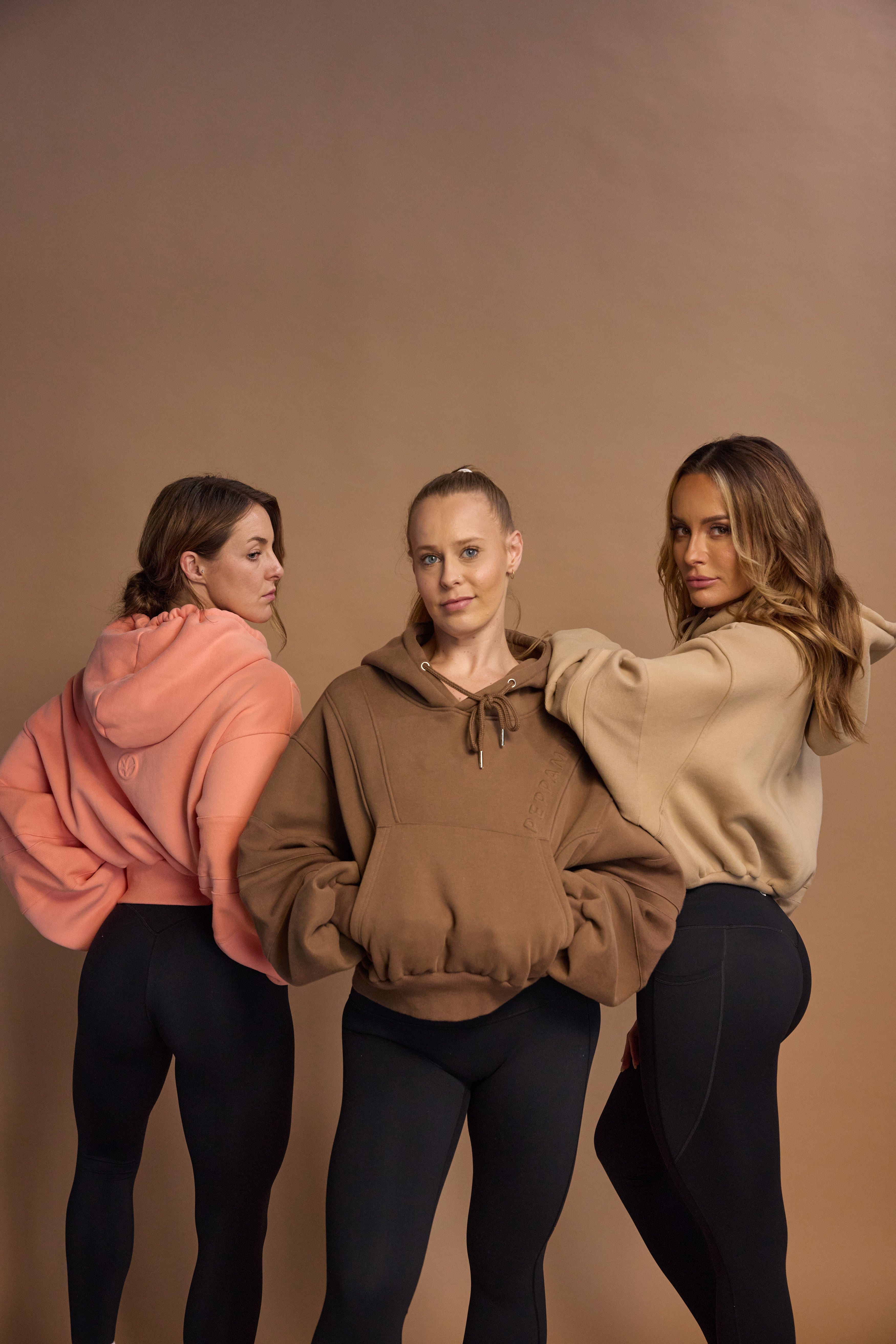 Oversize batwing hoodie, hip length, with slouchy oversized sleeves, piped seams, iconic ribbed panels and a kangaroo pocket with a hidden phone pocket inside in chocolate brown, coral and a beige sand colour