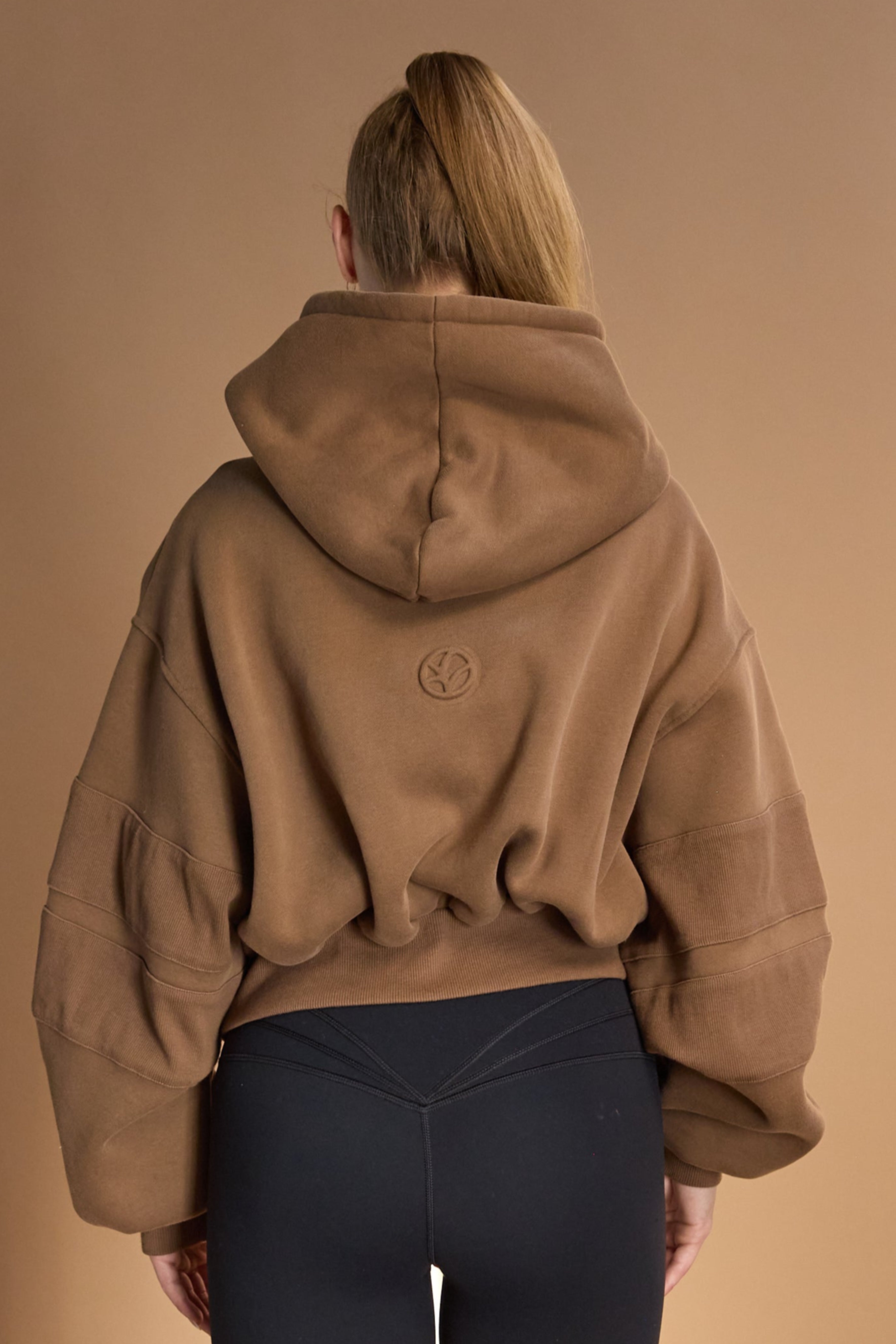 Oversize batwing hoodie, hip length, with slouchy oversized sleeves, piped seams, iconic ribbed panels and a kangaroo pocket with a hidden phone pocket inside in chocolate brown colour