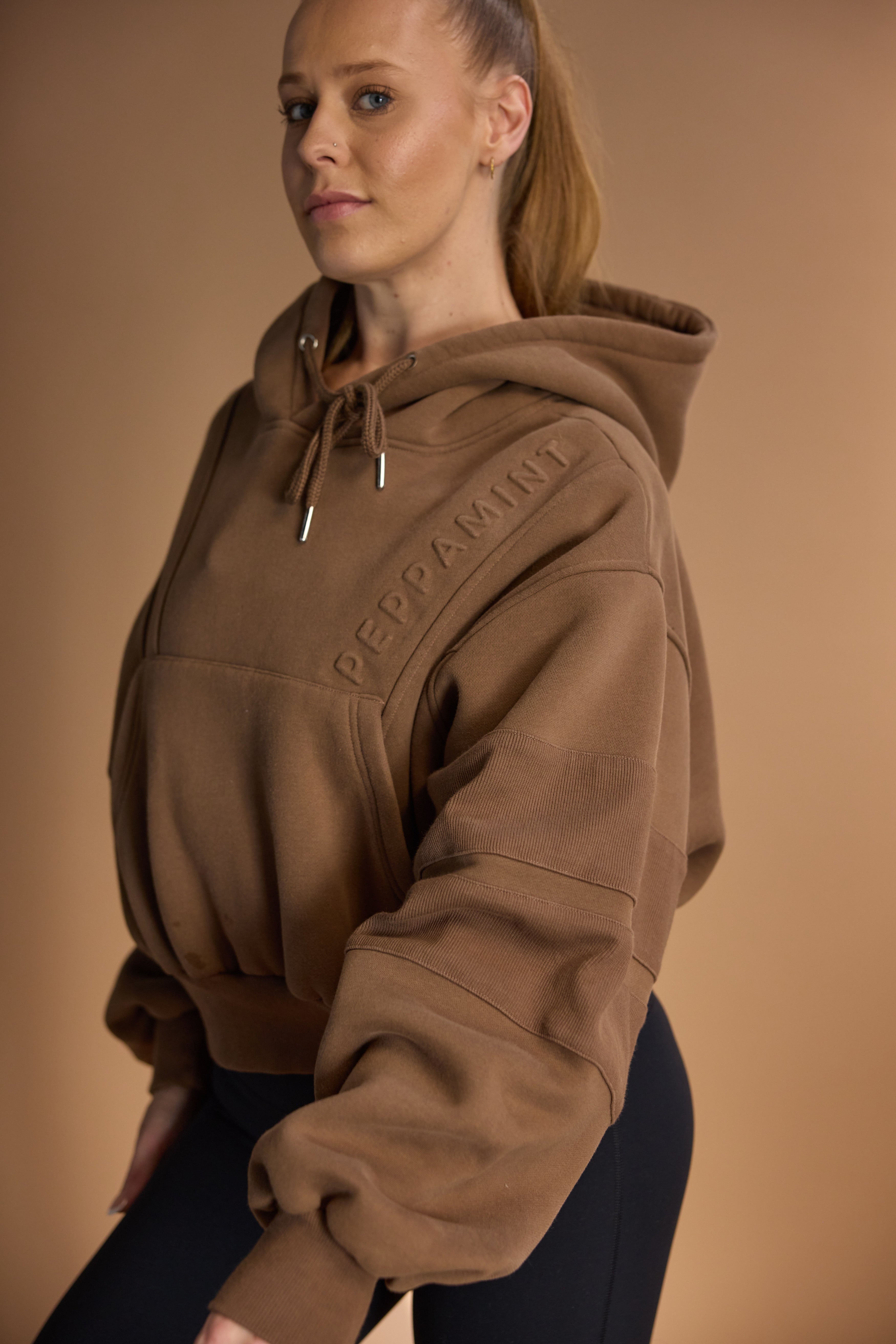 Oversize batwing hoodie, hip length, with slouchy oversized sleeves, piped seams, iconic ribbed panels and a kangaroo pocket with a hidden phone pocket inside in chocolate brown colour
