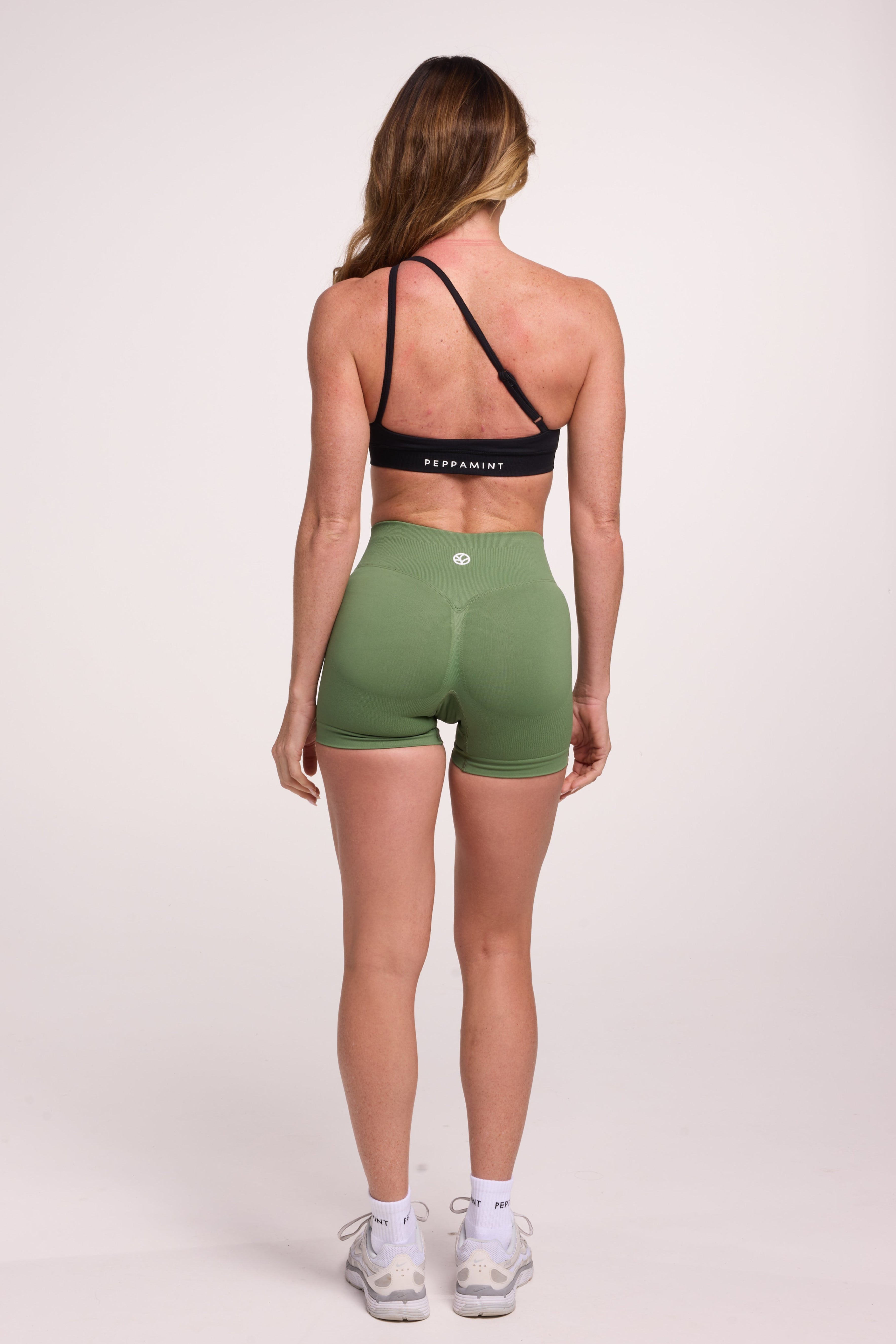 Front cross over strap activewear bra in seamless fabric with adjustable back straps, and ribbed supportive underbust band in black and seamless gym tights with booty contouring panels, invisible scrunch technology, sweetheart shaped back seams and thick supportive fabric in mermaid green