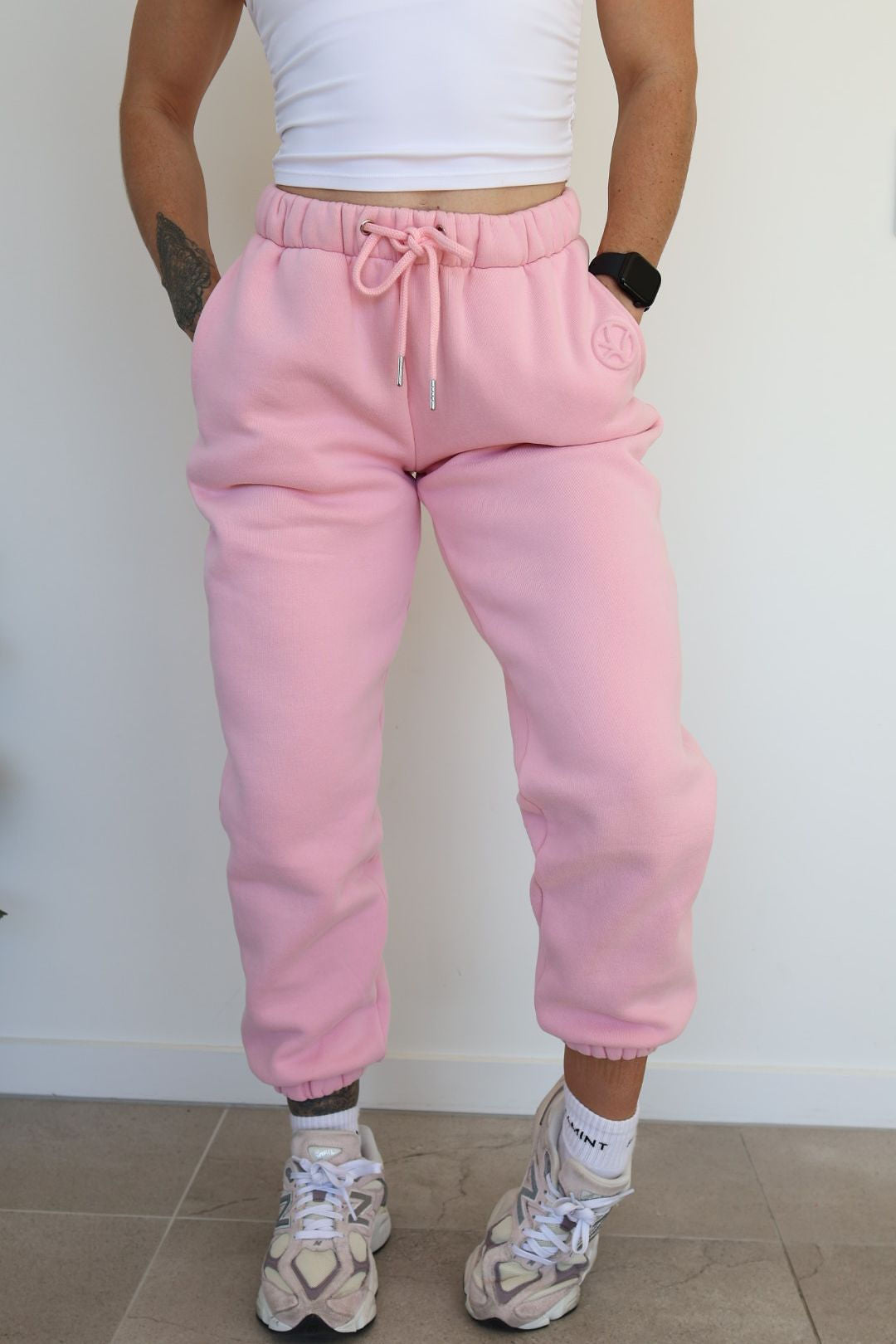 Fleece lined joggers in baby pink with elasticated waistband, drawstring, two side pockets and a subtle embossed logo icon on left pocket