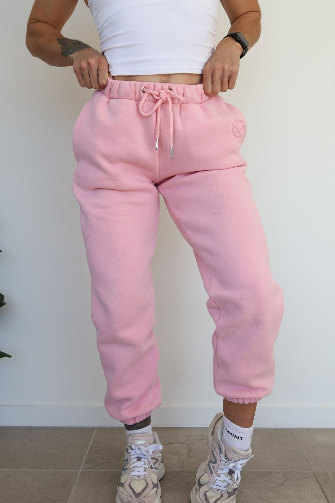 Fleece lined joggers in baby pink with elasticated waistband, drawstring, two side pockets and a subtle embossed logo icon on left pocket