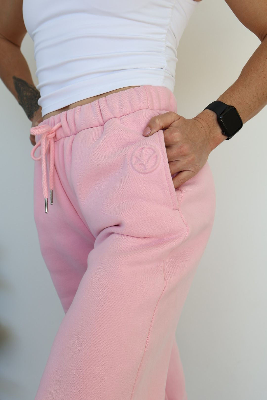 Fleece lined joggers in baby pink with elasticated waistband, drawstring, two side pockets and a subtle embossed logo icon on left pocket