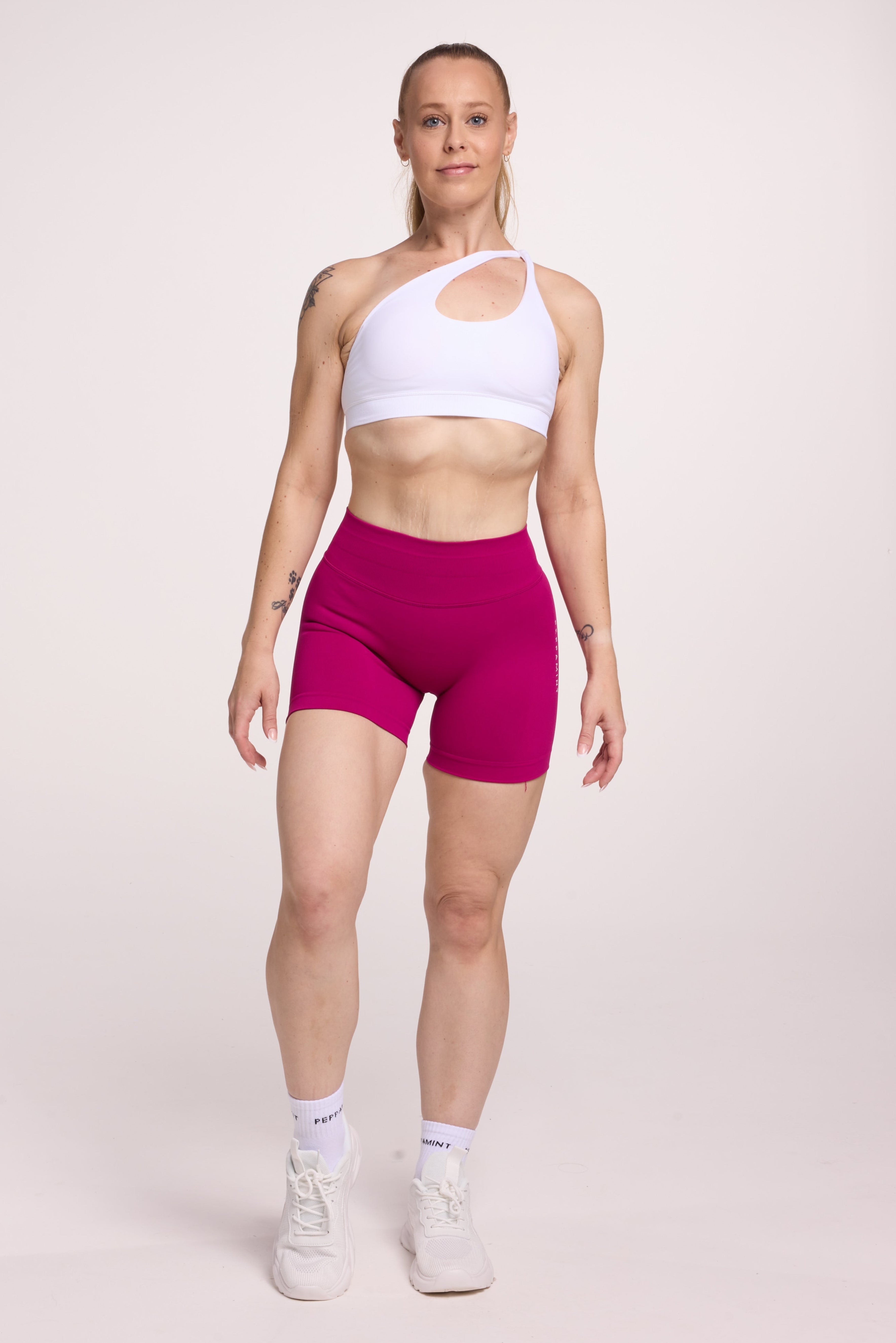 Front cross over strap activewear bra in seamless fabric with adjustable back straps, and ribbed supportive underbust band in white and seamless gym tights with booty contouring panels, invisible scrunch technology, sweetheart shaped back seams and thick supportive fabric in magenta pink